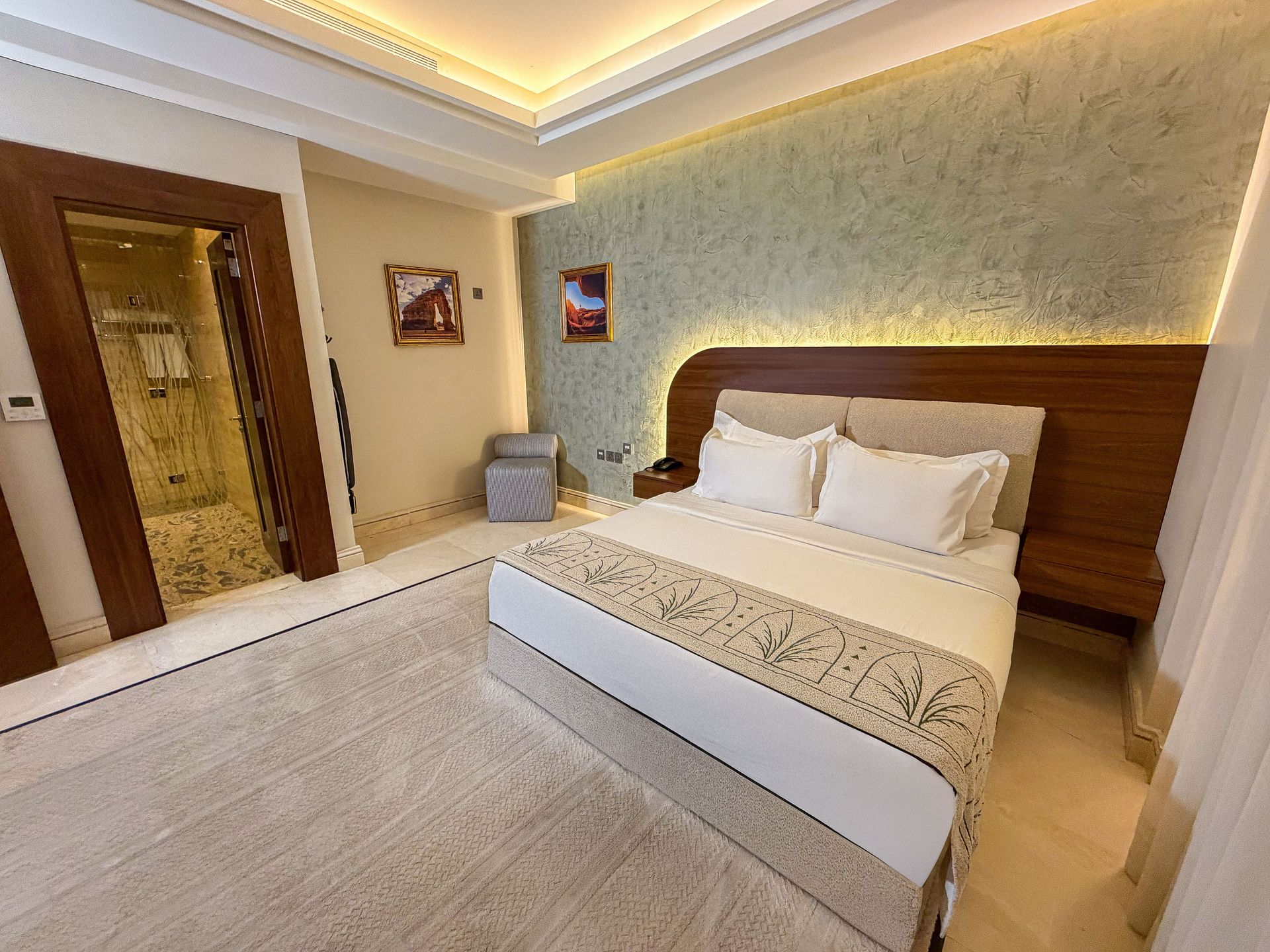 Modern hotel bedroom with a large bed, wood headboard, and warm ceiling lighting