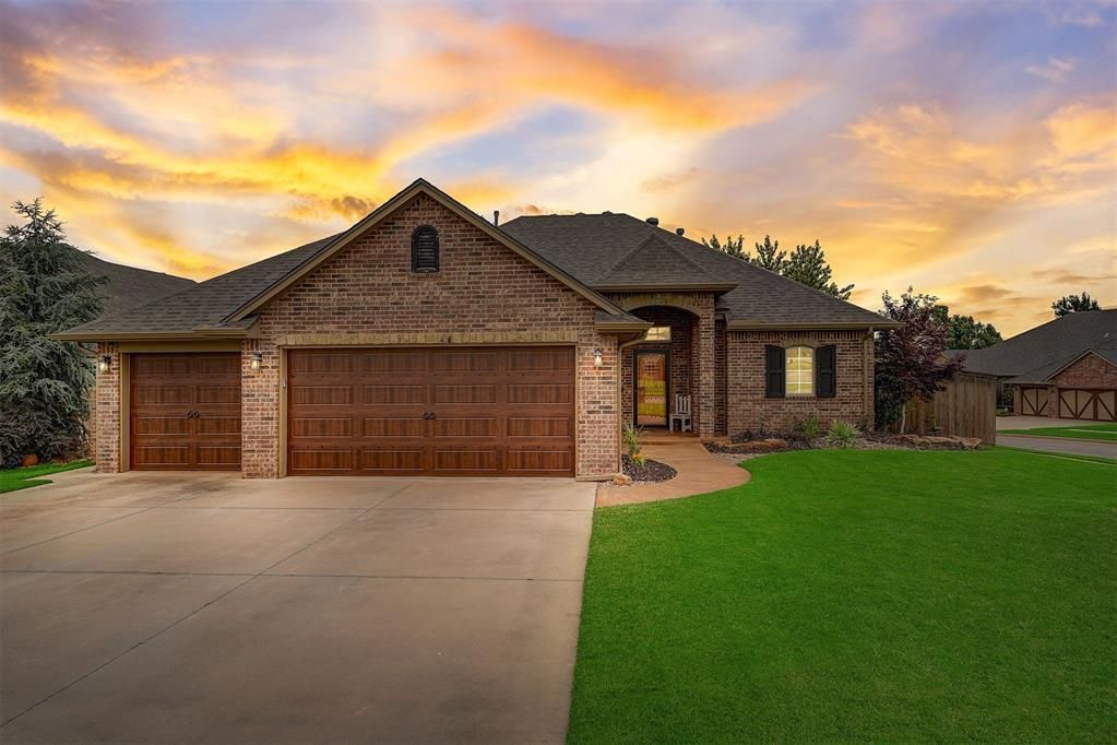 A large brick house with three garage doors and a lush green lawn.