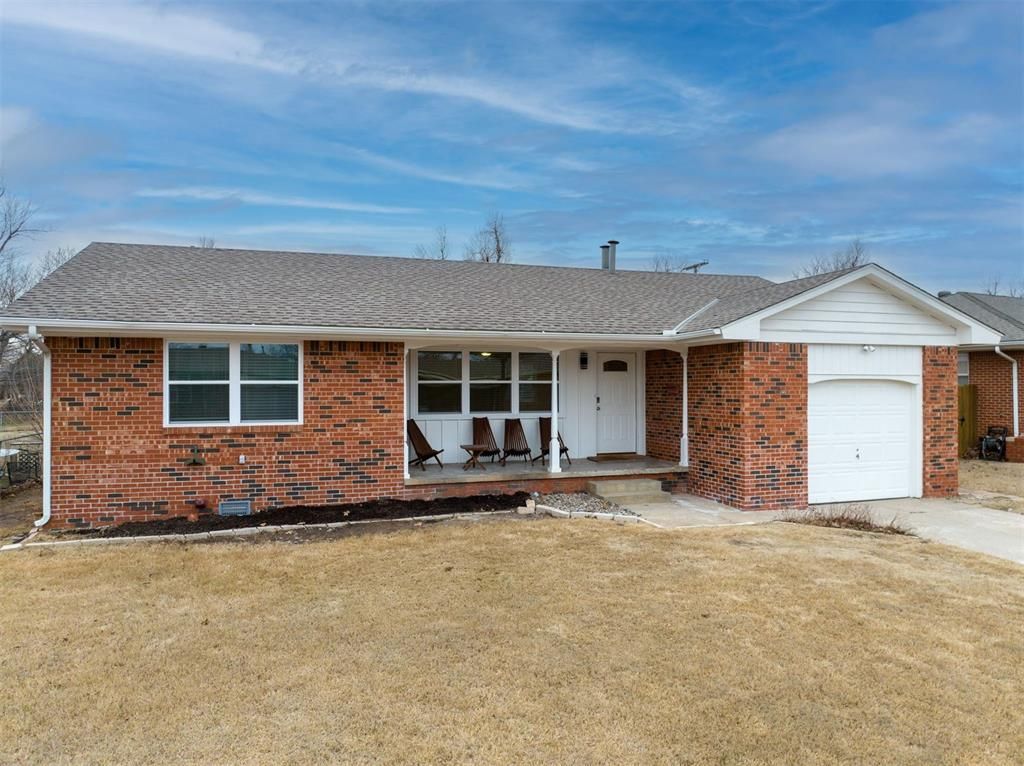 A brick house with a white garage and a porch with chairs.