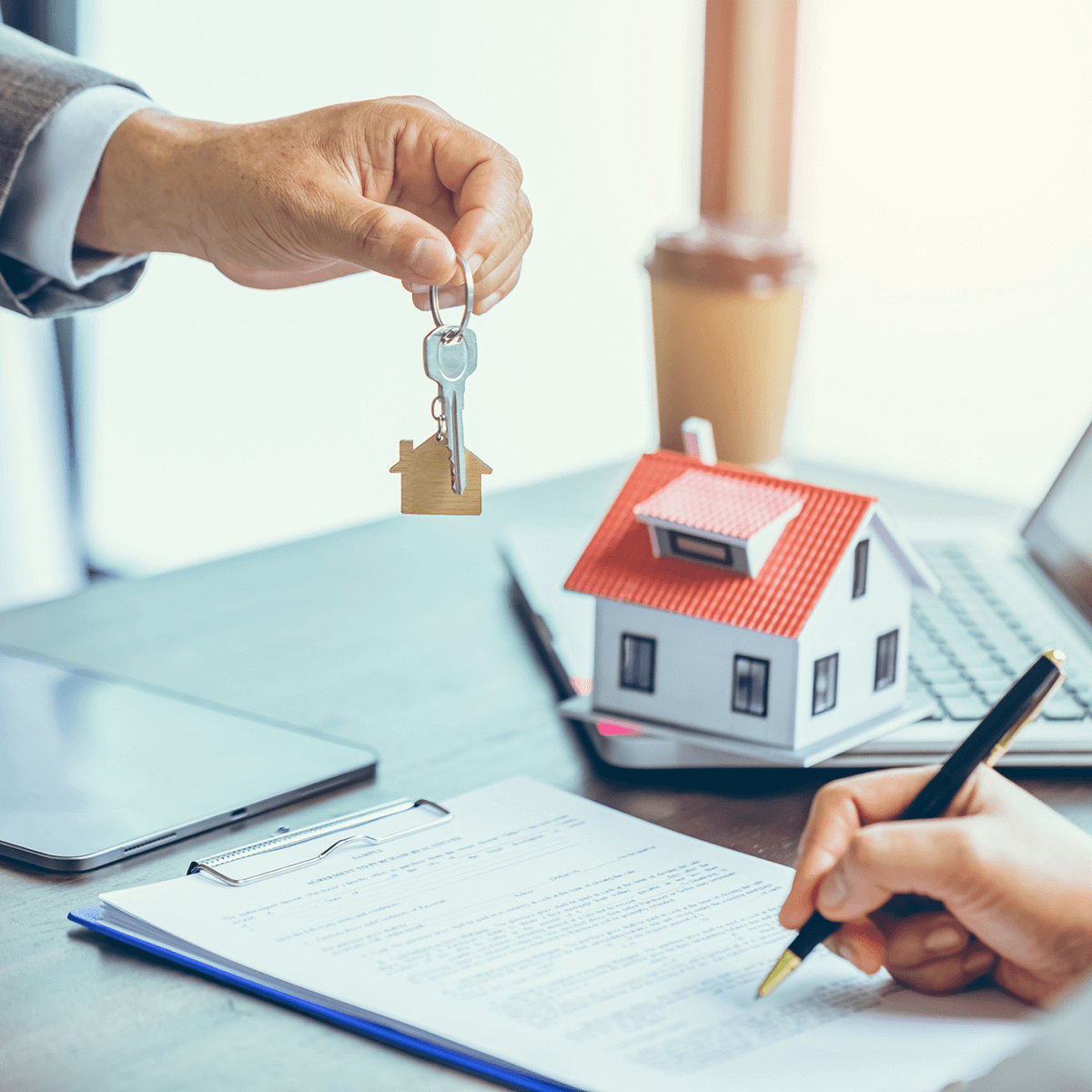 Una persona está firmando un documento junto a una maqueta de casa y unas llaves.