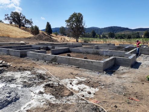 A man is standing in a dirt field next to a concrete foundation.