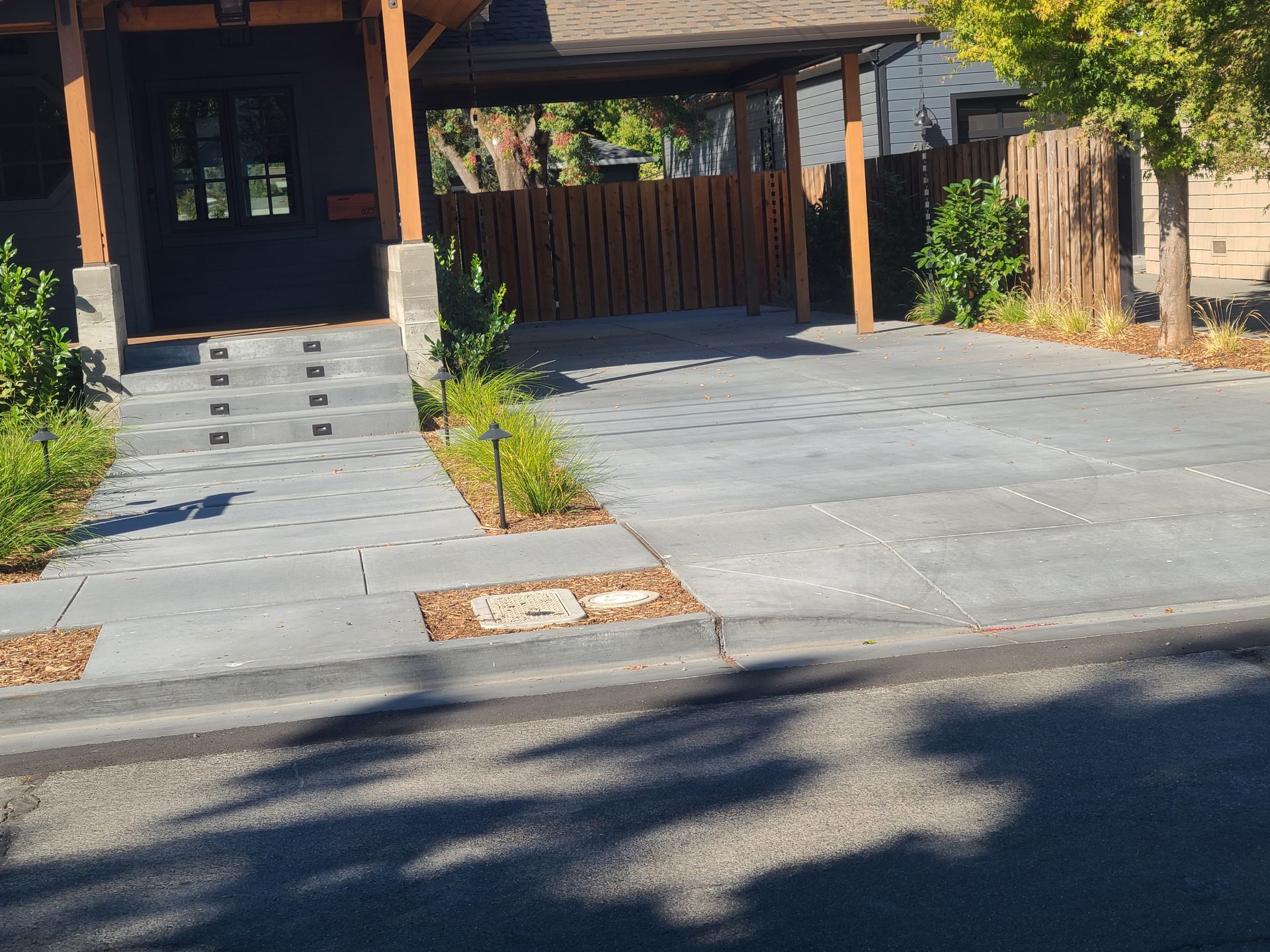 A concrete driveway leading to a house with a wooden fence