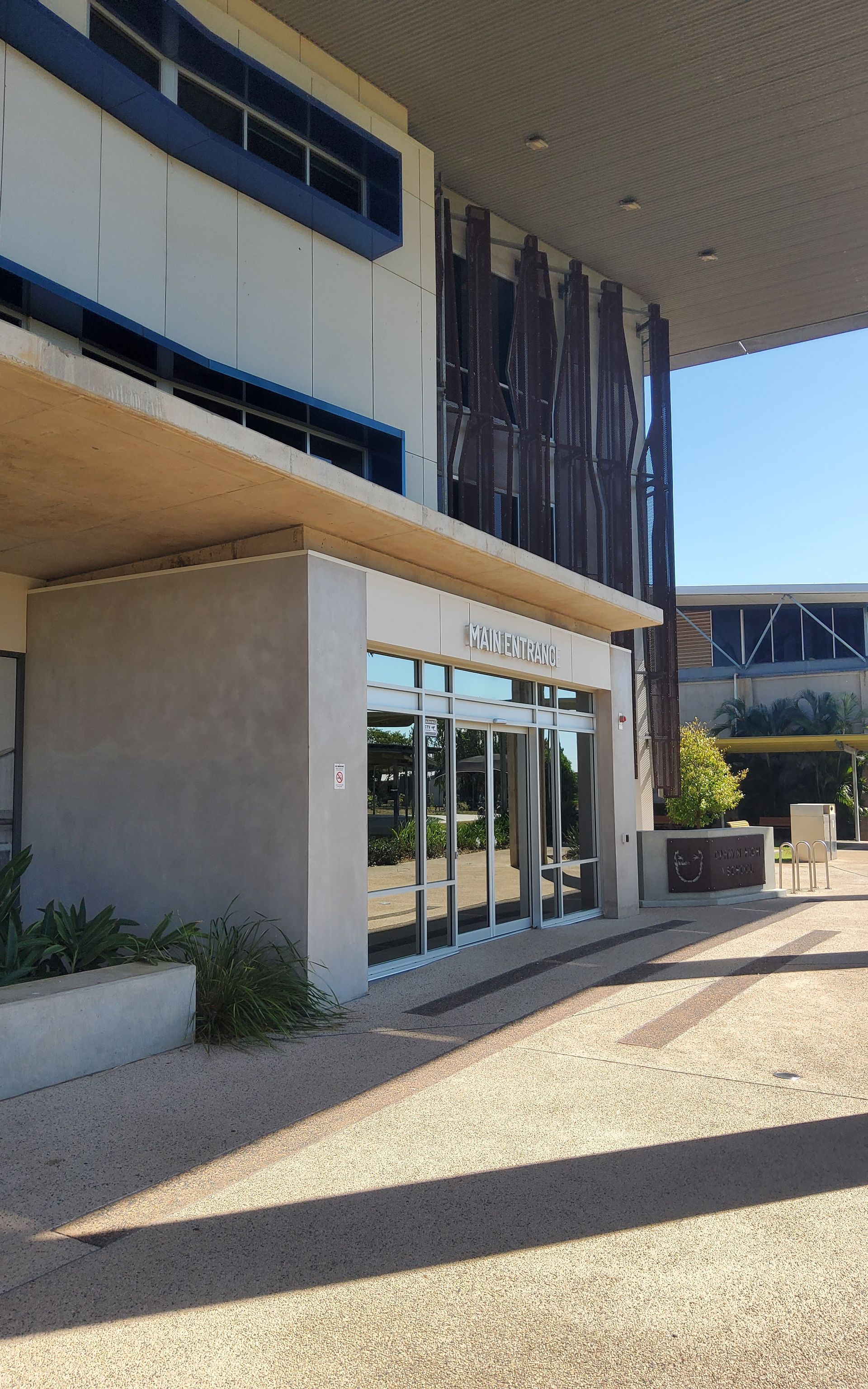 Modern building entrance with glass doors under a tan overhang and blue accents — Neil Griffiths Rendering in Berry Springs, NT