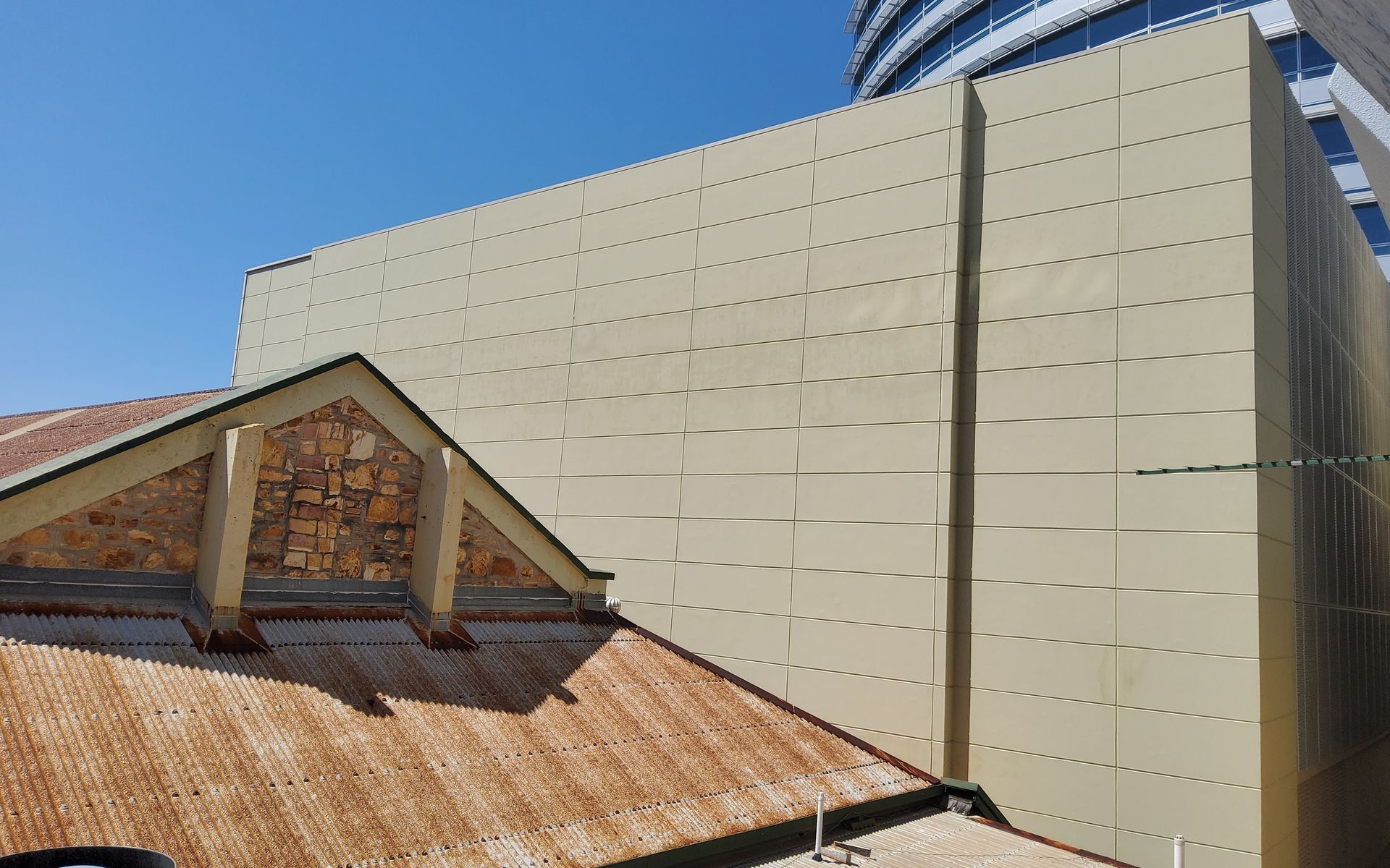 Beige building facade behind a rusty, old roof and gable against a blue sky   — Neil Griffiths Rendering in Berry Springs, NT