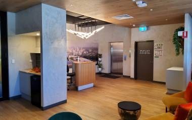 Modern hotel lobby with reception desk, elevator, seating, and a decorative light fixture — Neil Griffiths Rendering in Berry Springs, NT