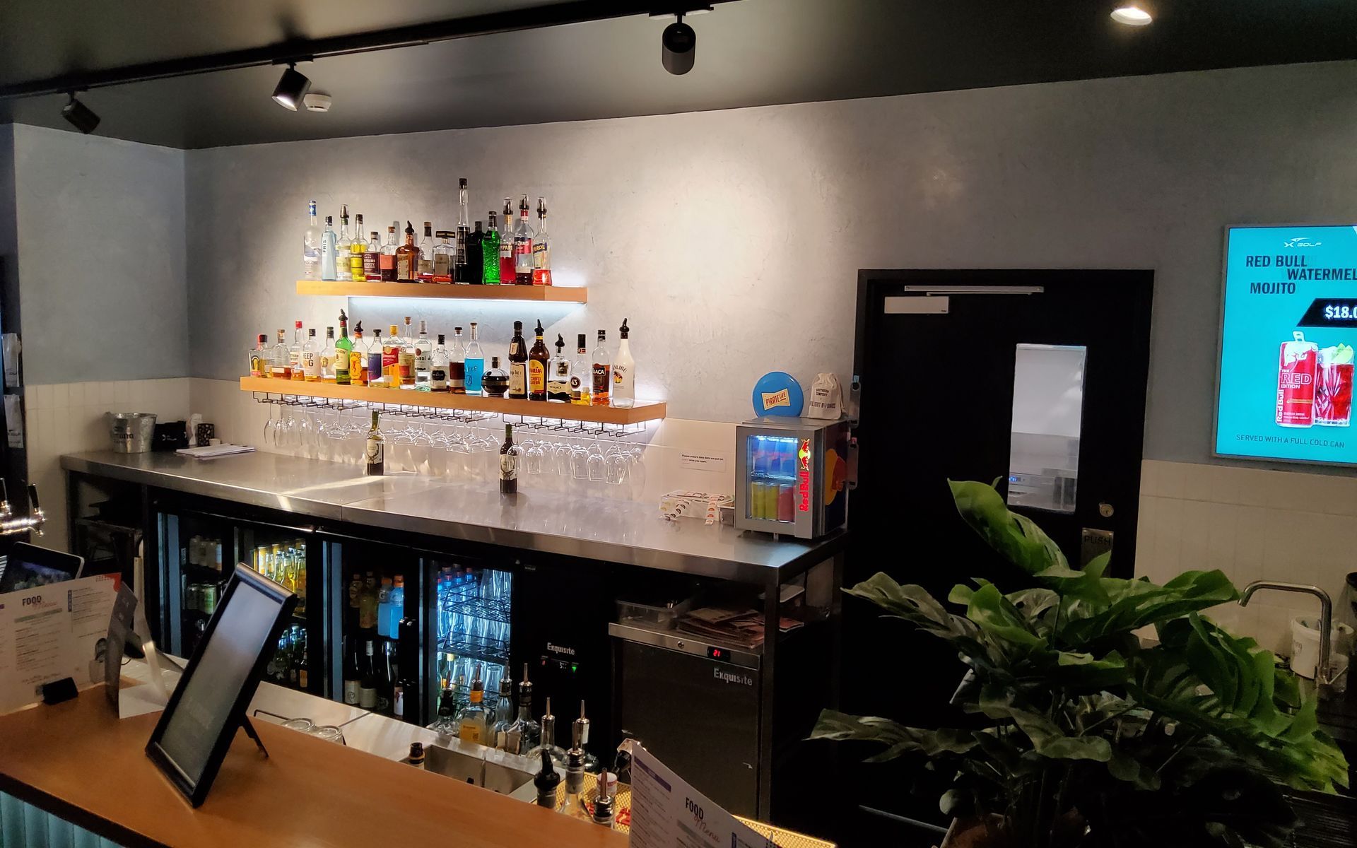 Bar with bottles, shelves, stainless steel counter, beer fridges, and a plant — Neil Griffiths Rendering in Berry Springs, NT