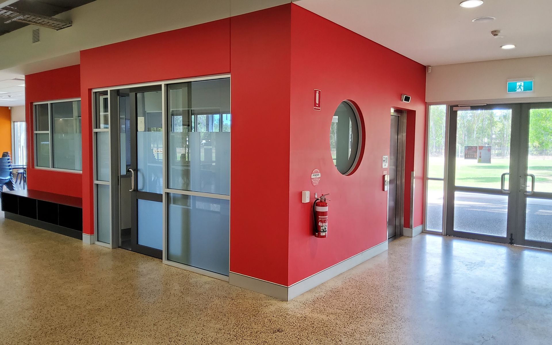 Red-walled Hallway With a Fire Extinguisher, a Round Window, and Glass Doors Leading Outside — Neil Griffiths Rendering in Berry Springs, NT