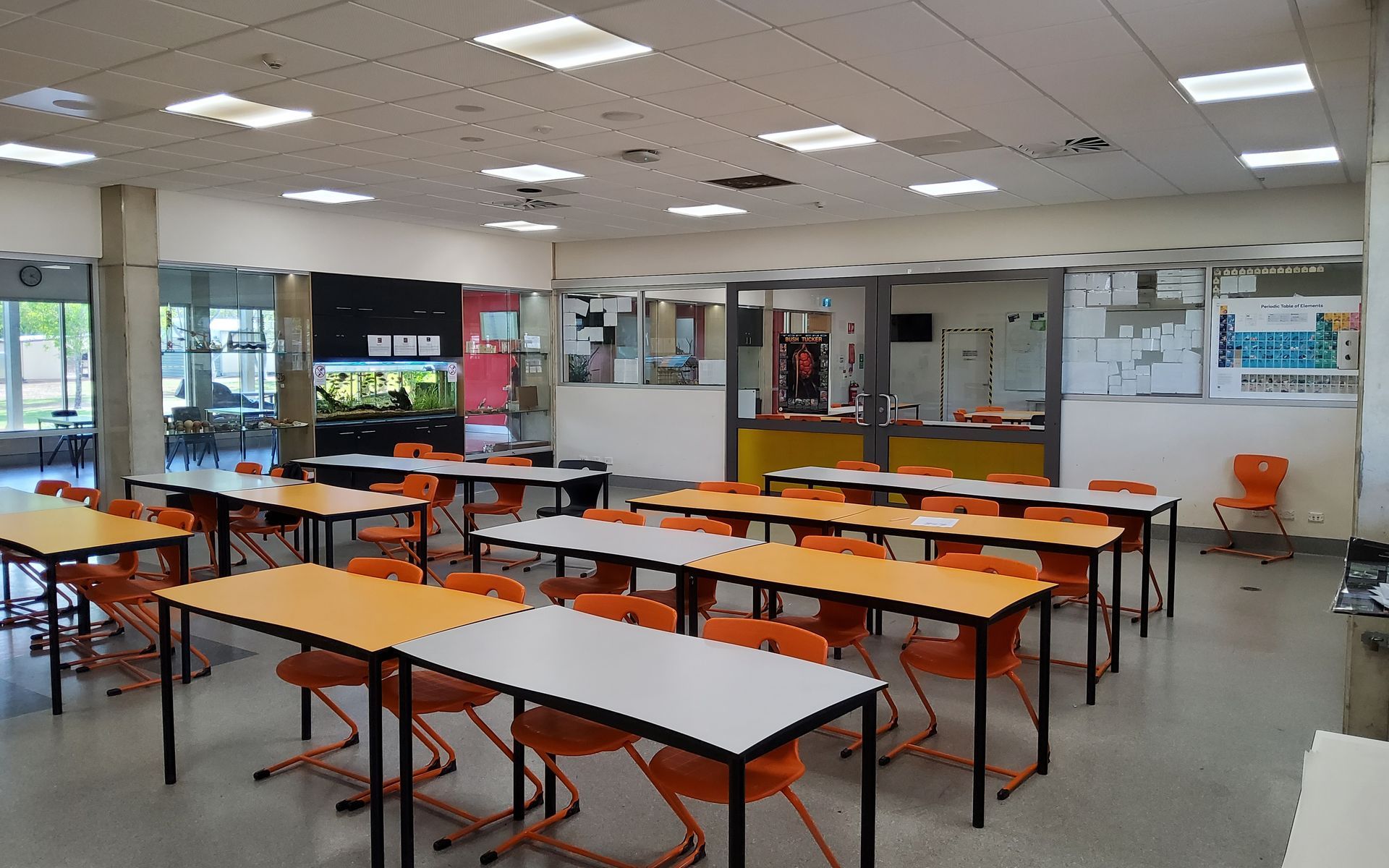 An Empty Classroom With Orange Chairs and Desks. a Black, Orange, and White Wall With a Window is at the Back — Neil Griffiths Rendering in Berry Springs, NT