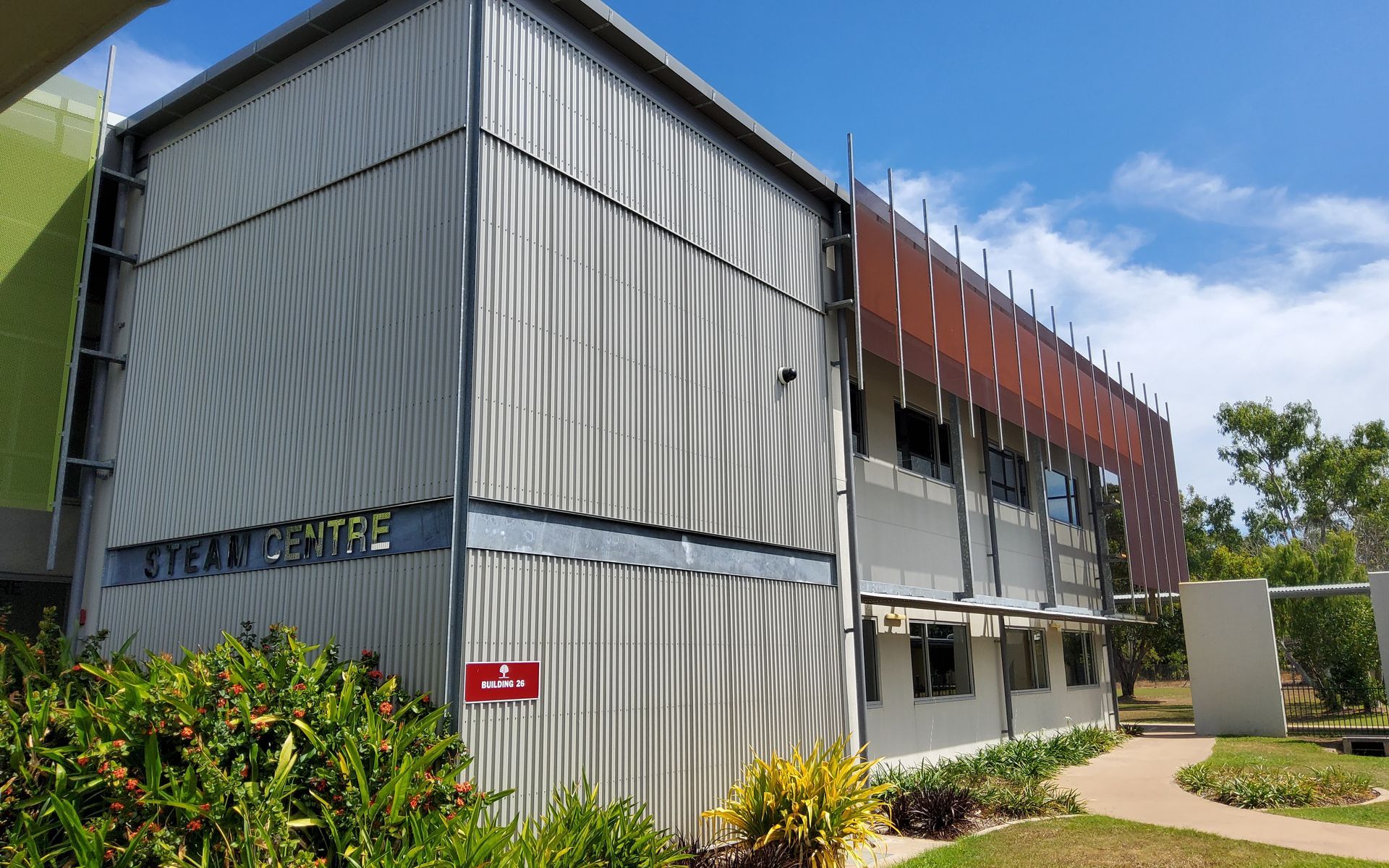 STEAM Centre Building With Corrugated Silver Siding, Brown Screening, and Greenery Against a Blue Sky  — Neil Griffiths Rendering in Berry Springs, NT