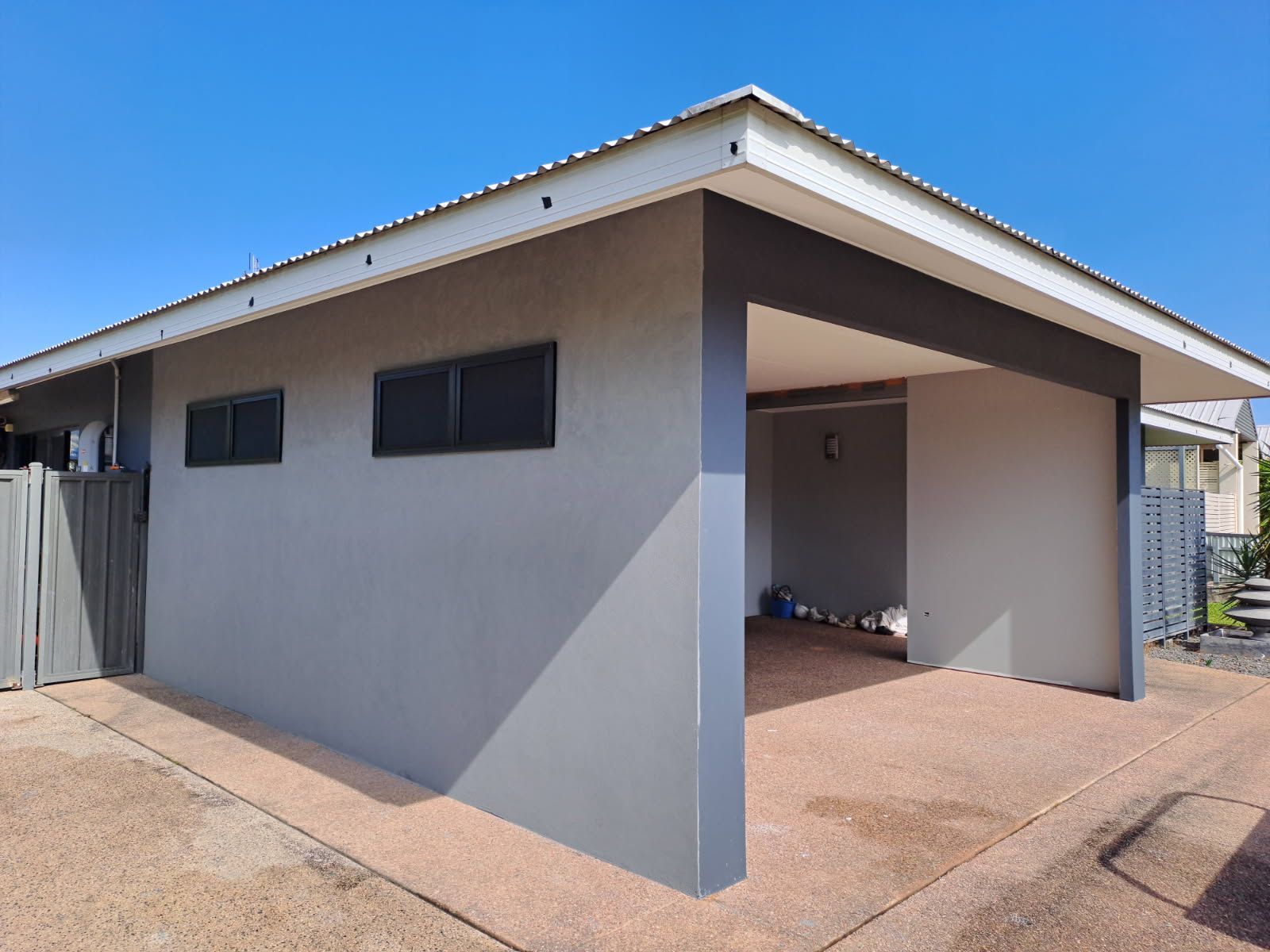Gray and white carport with a flat roof, built into a building; blue sky   — Neil Griffiths Rendering in Berry Springs, NT