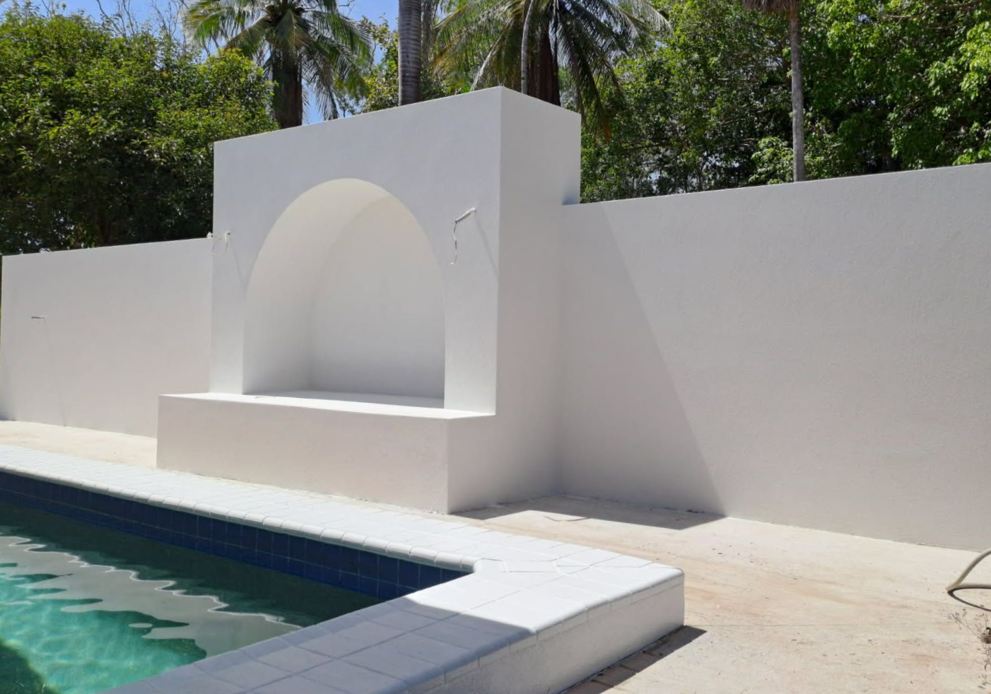 White pool wall with an arched alcove and pool in the foreground. Green foliage in the background   — Neil Griffiths Rendering in Berry Springs, NT