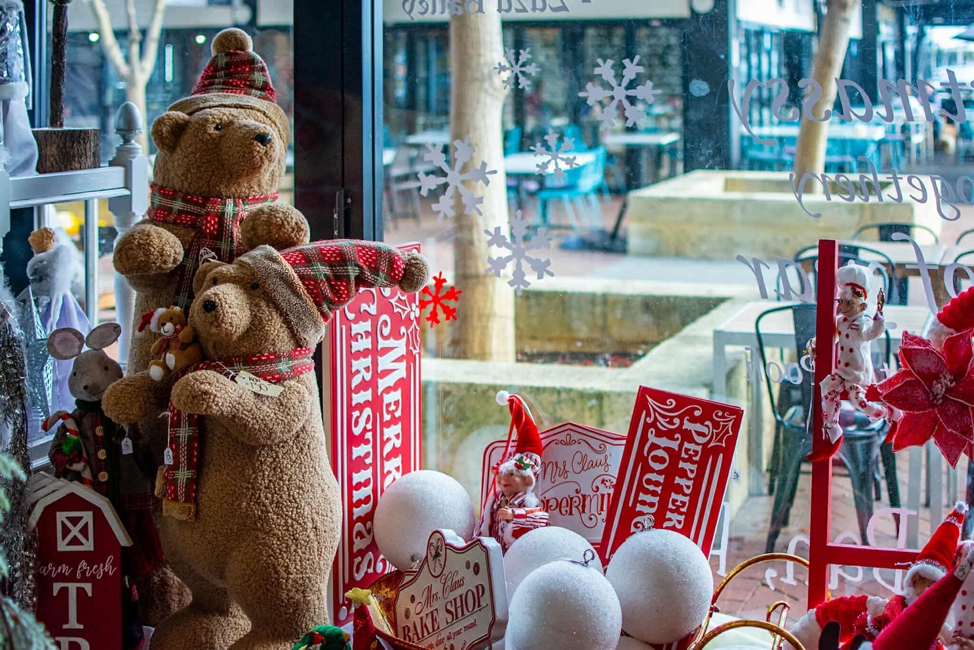 A display of christmas decorations in a store window with a teddy bear wearing a santa hat.