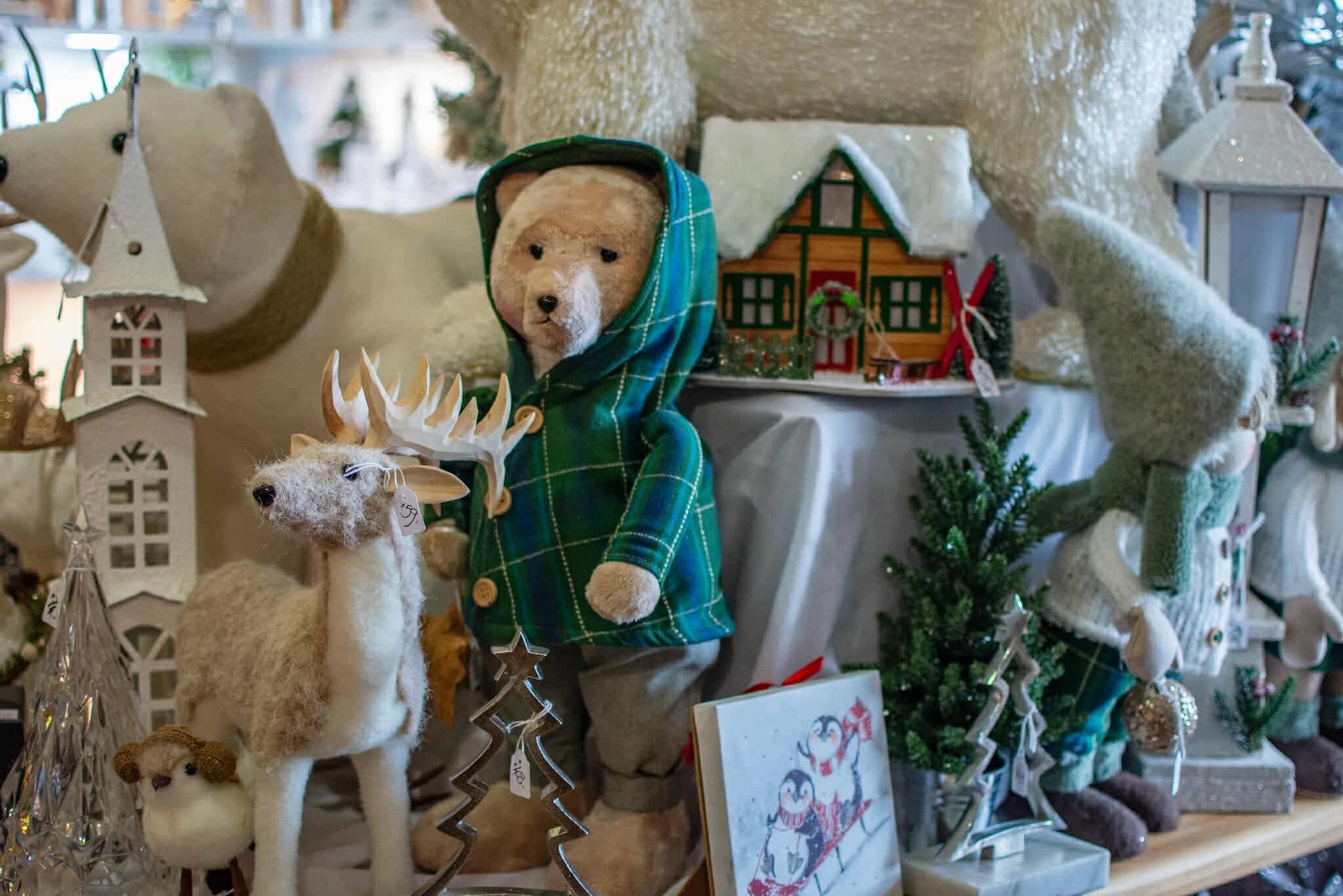 A teddy bear in a green jacket is surrounded by christmas decorations.