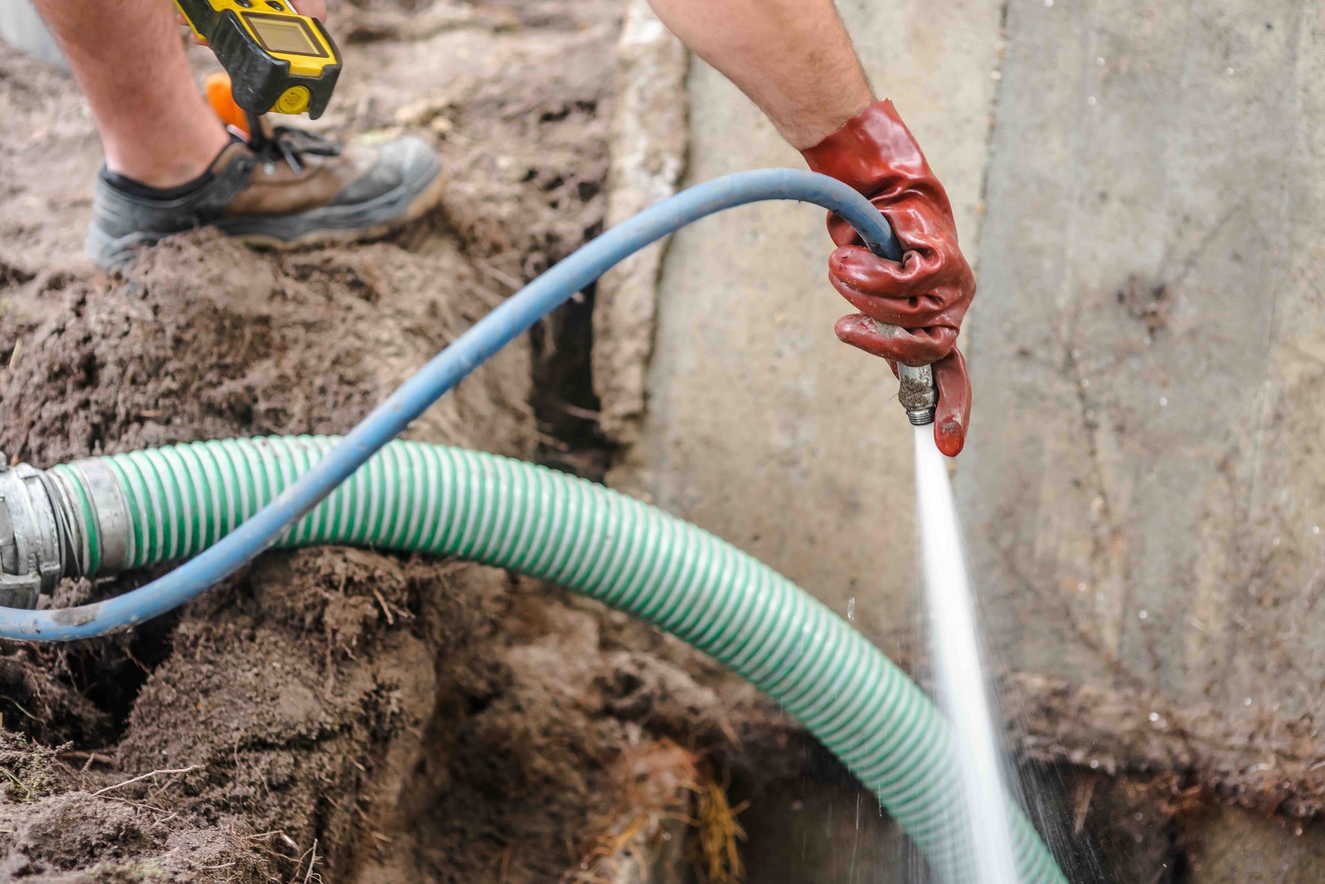a person spraying water into a septic tank out of a high pressure hose.