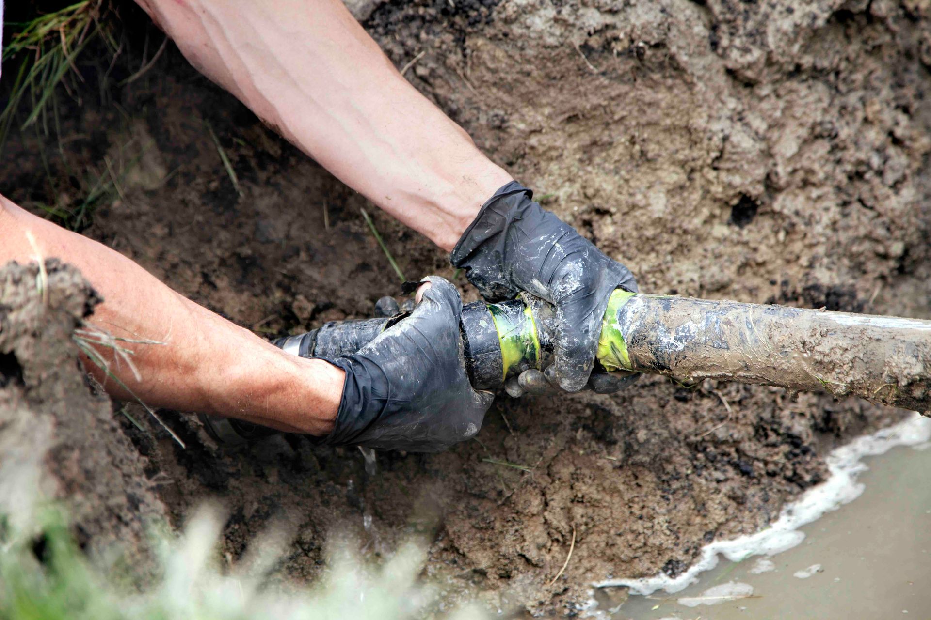a person attaching two pipes together in mud with water by them.