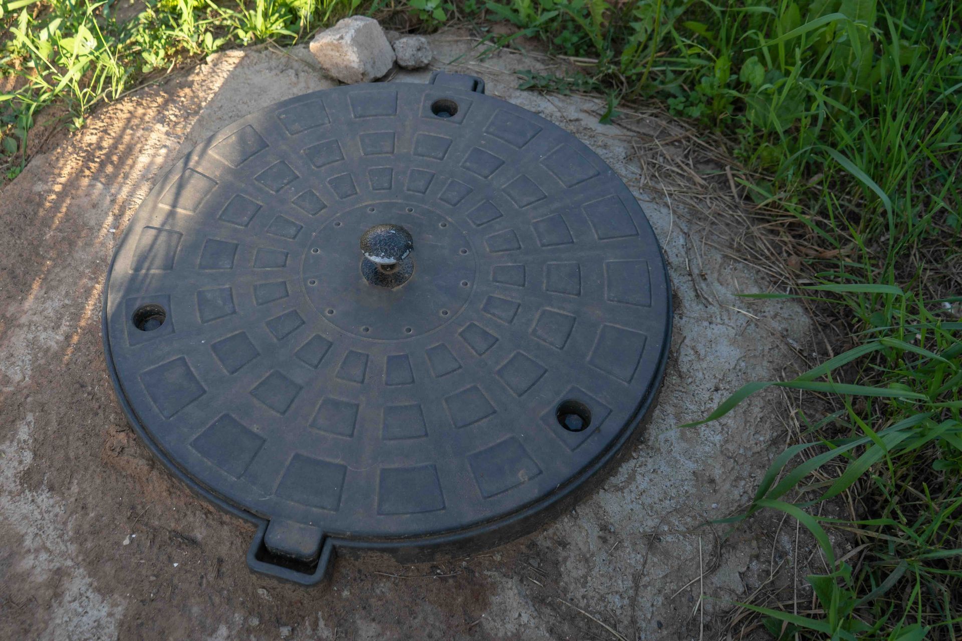 A septic tank lid on top of a pile of dirt.