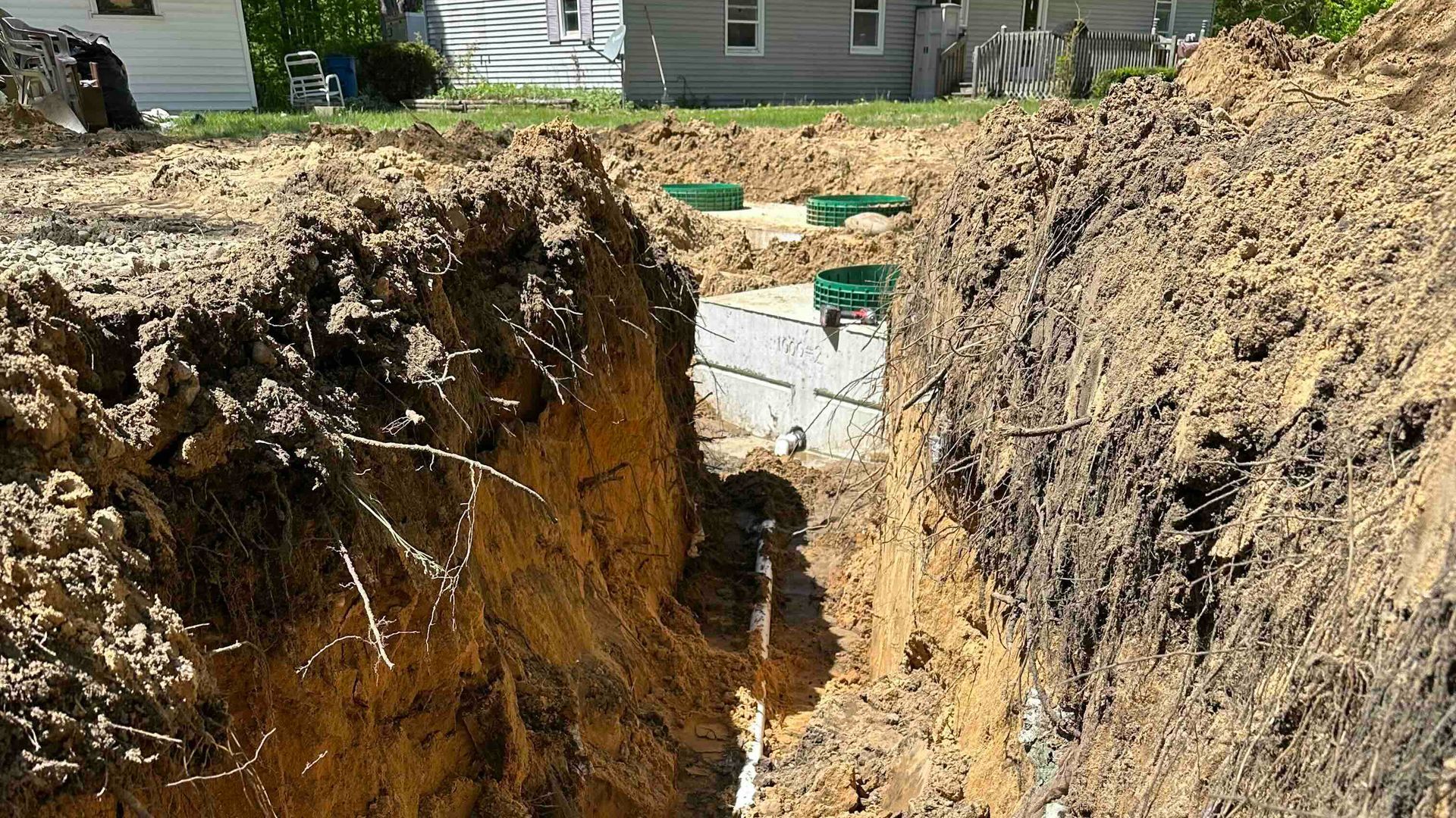 A large hole in the ground with a pipe from a septic tank and a house in the background.