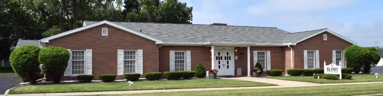 A single-story, red brick office building with a grey shingled roof, white shutters, and a central white double door.