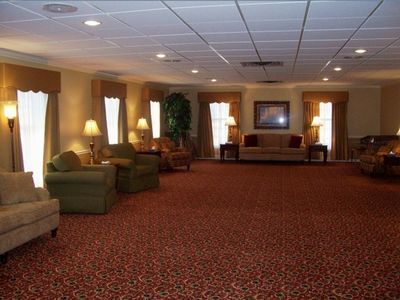 A carpeted lounge area with armchairs and sofas, arranged near windows with draped curtains and lamps.
