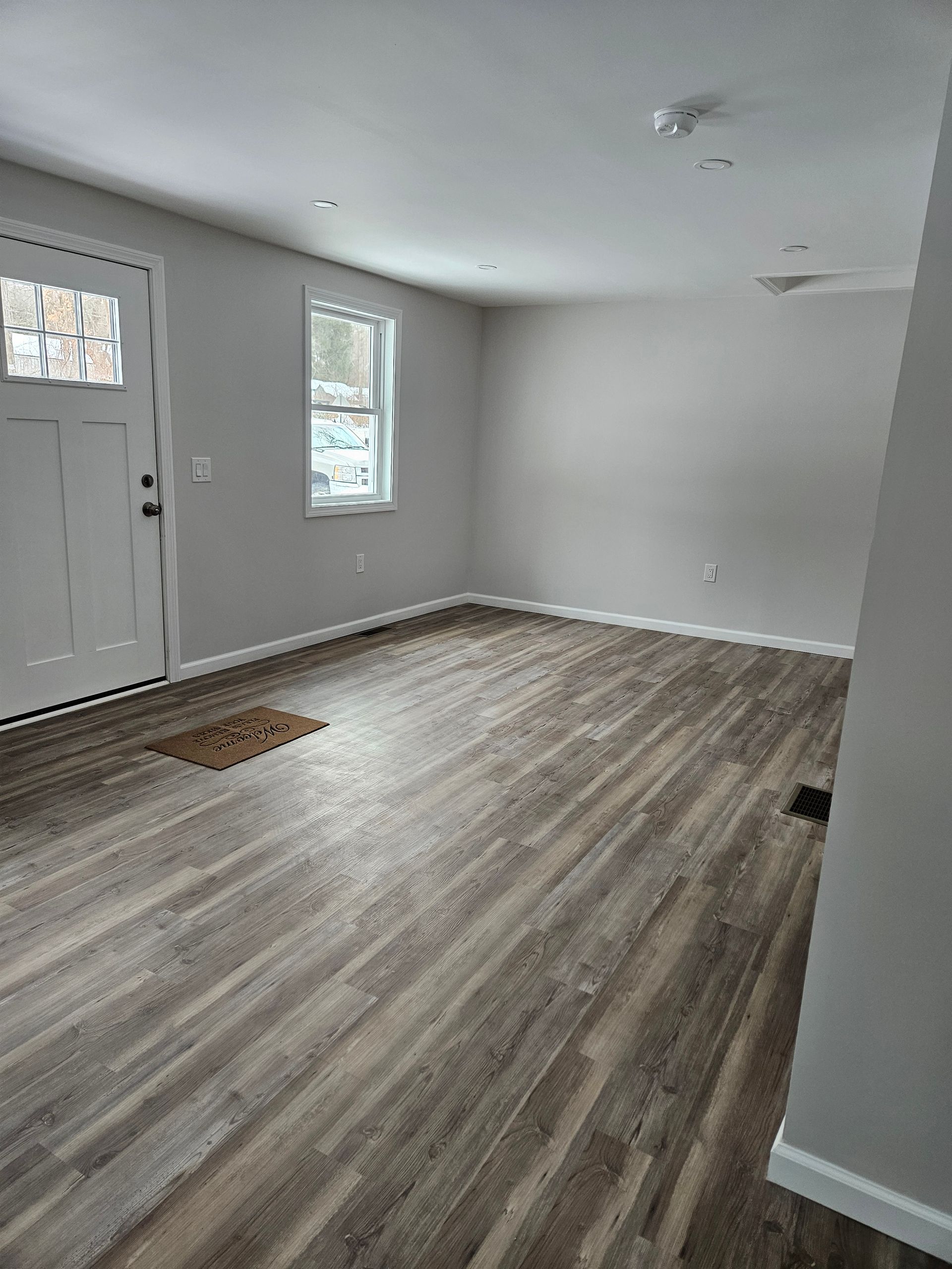 Empty room with wood-look floor, white door, small window, and grey walls.