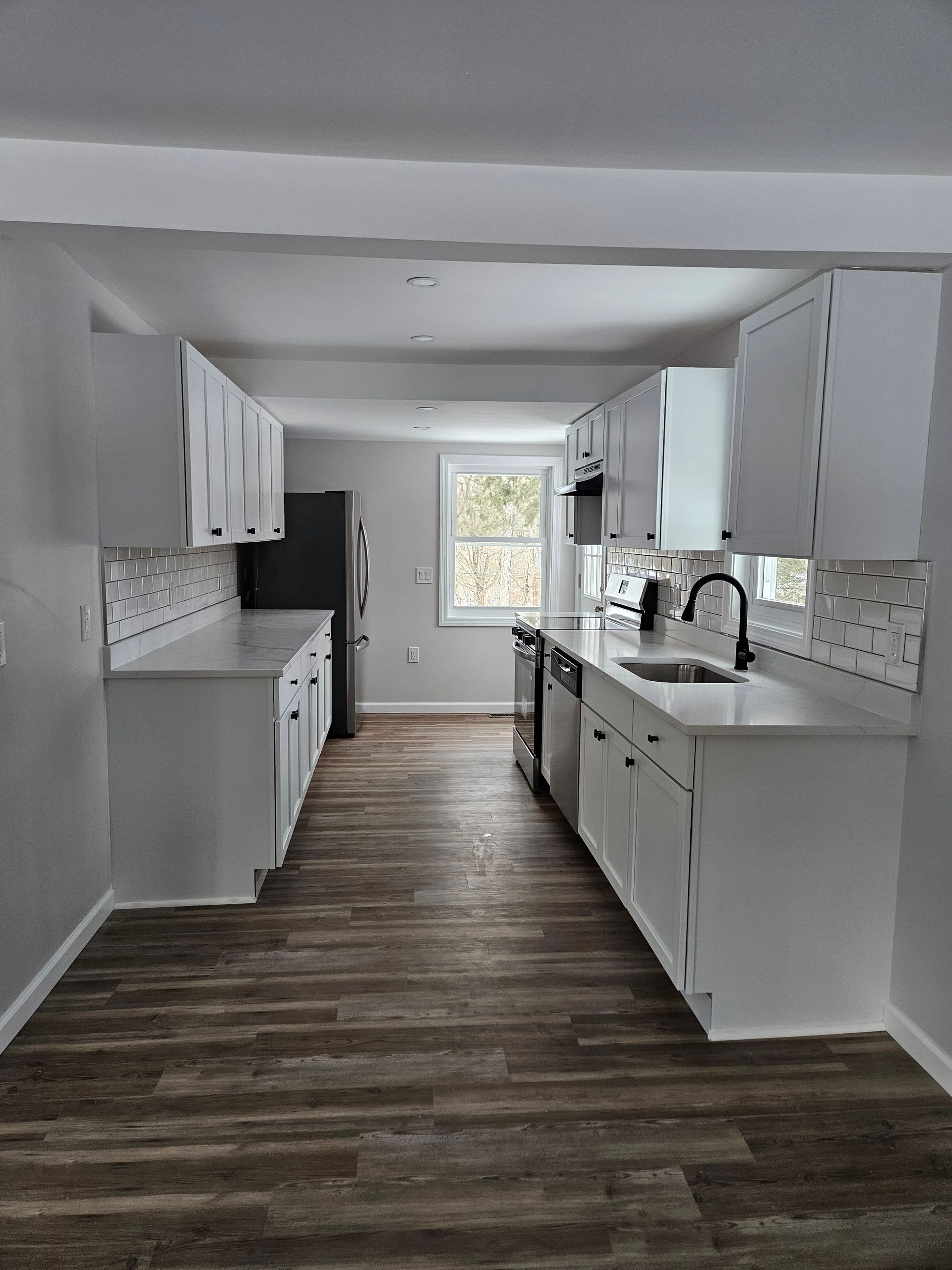 White kitchen with matching cabinets and countertops, stainless steel appliances, and wood-look flooring.