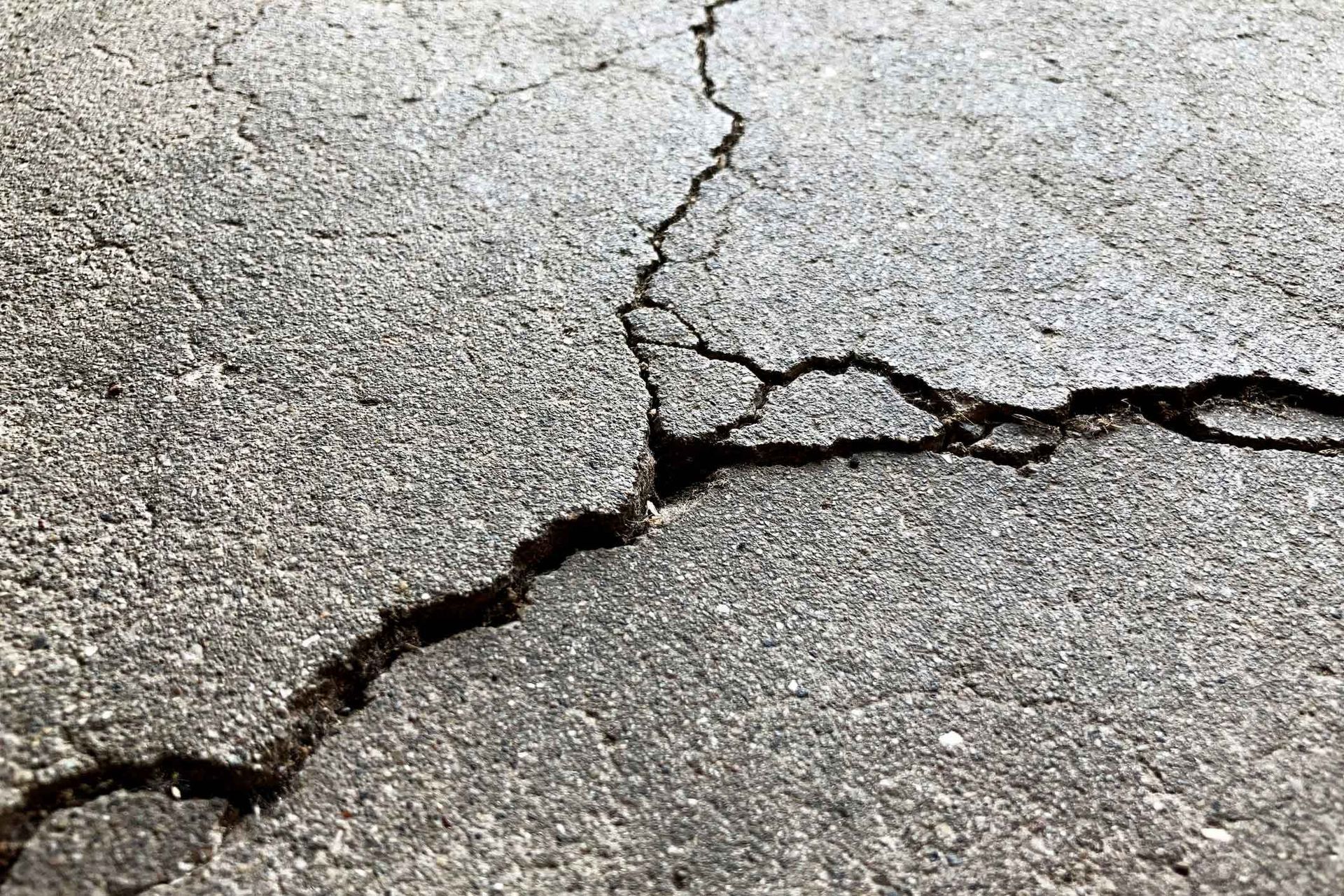 Cracked asphalt, showing deep fissures on a gray surface.