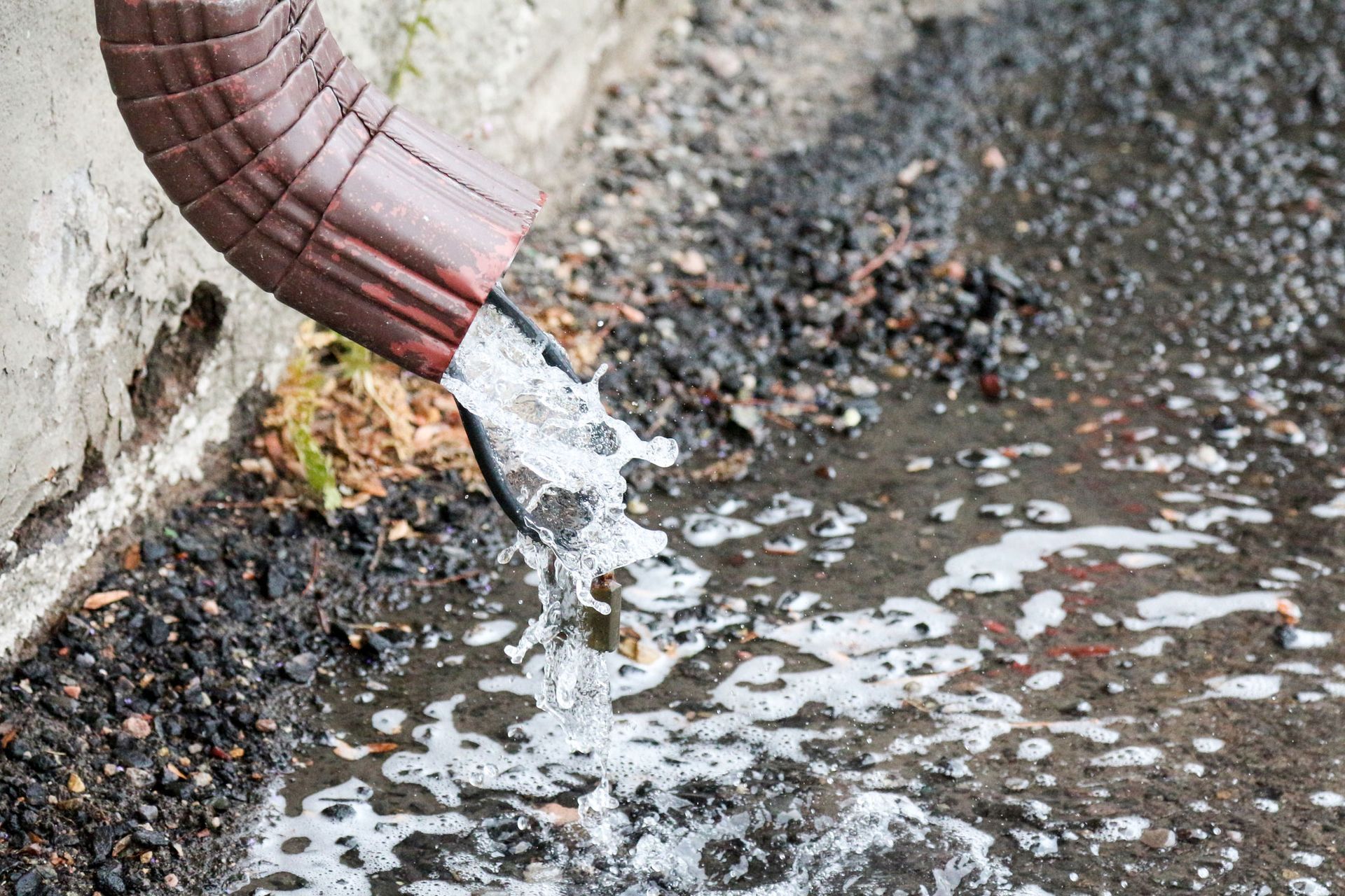 Brown gutter expelling water onto a dark asphalt surface.