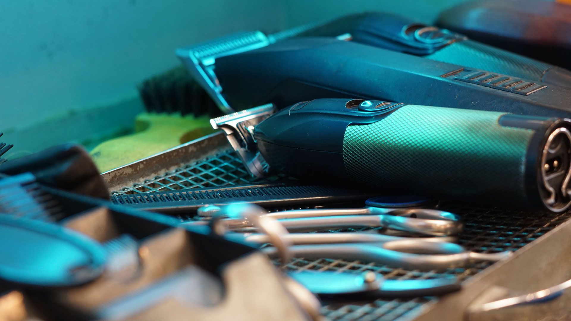 An array of barber tools under UV light including scissors, combs, brushes, and electric clippers.