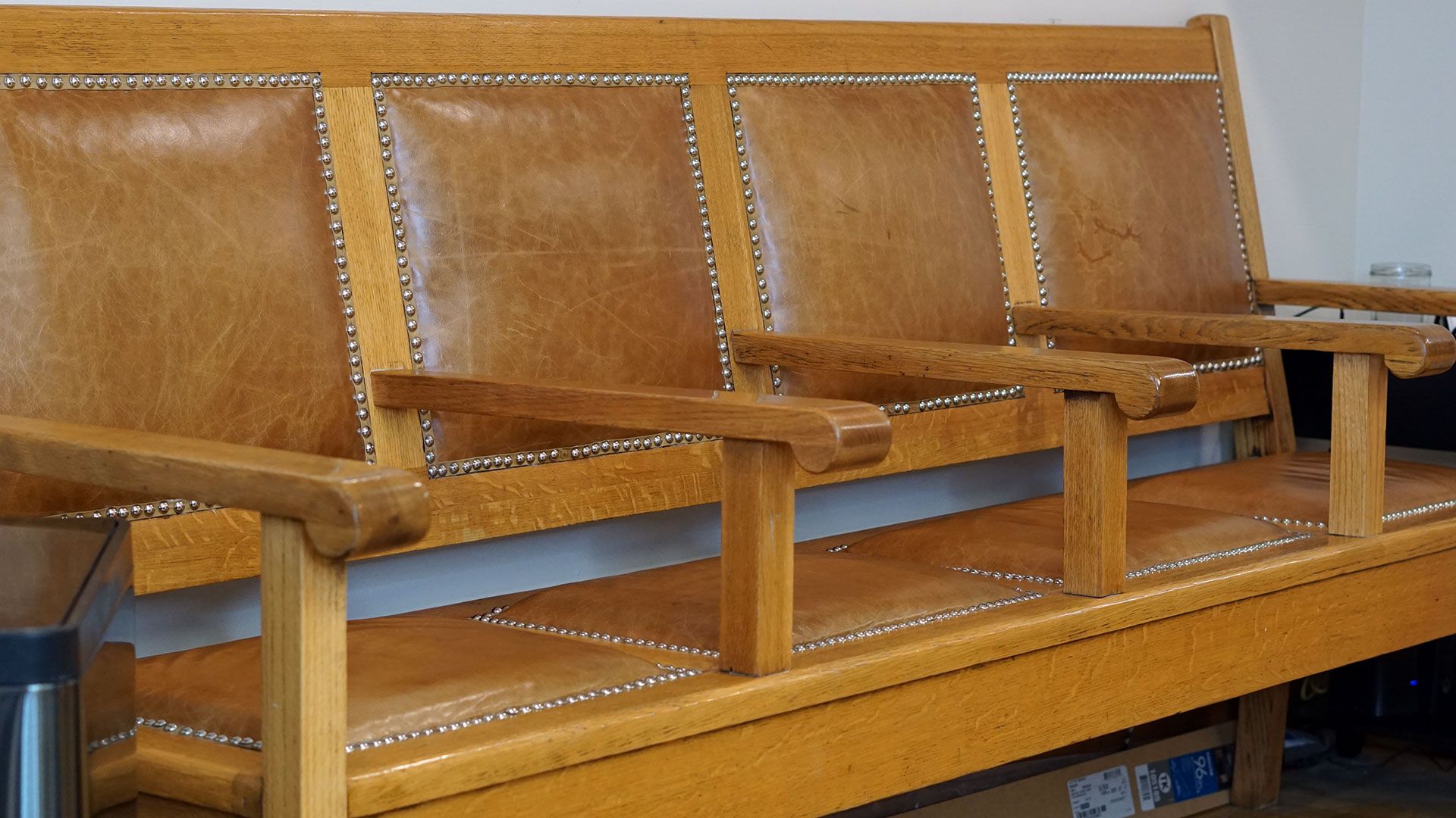 A bench built with solid oak and upholstered in brown leather in the waiting area of a barber shop called The Harbor Barber.