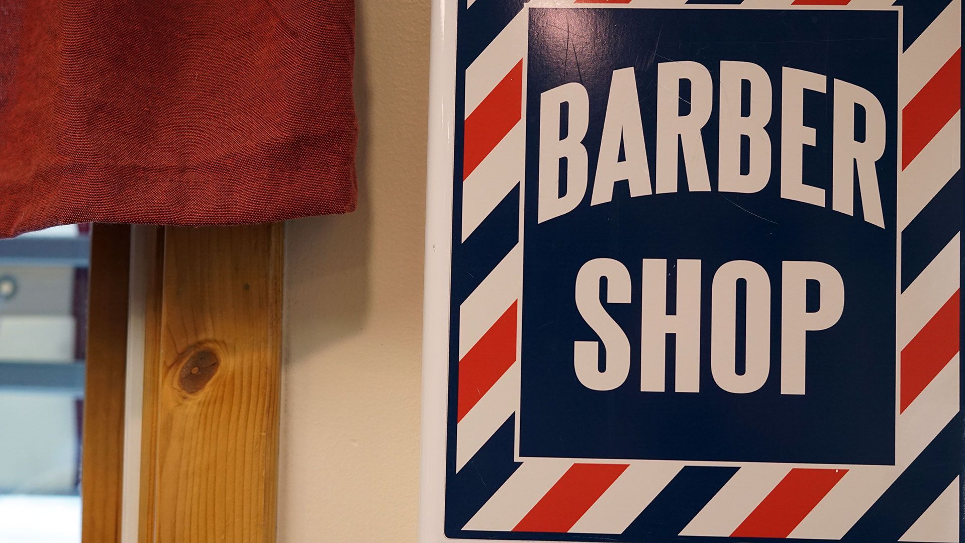 An antique red, white, and blue sign on the wall of a traditional barbershop.