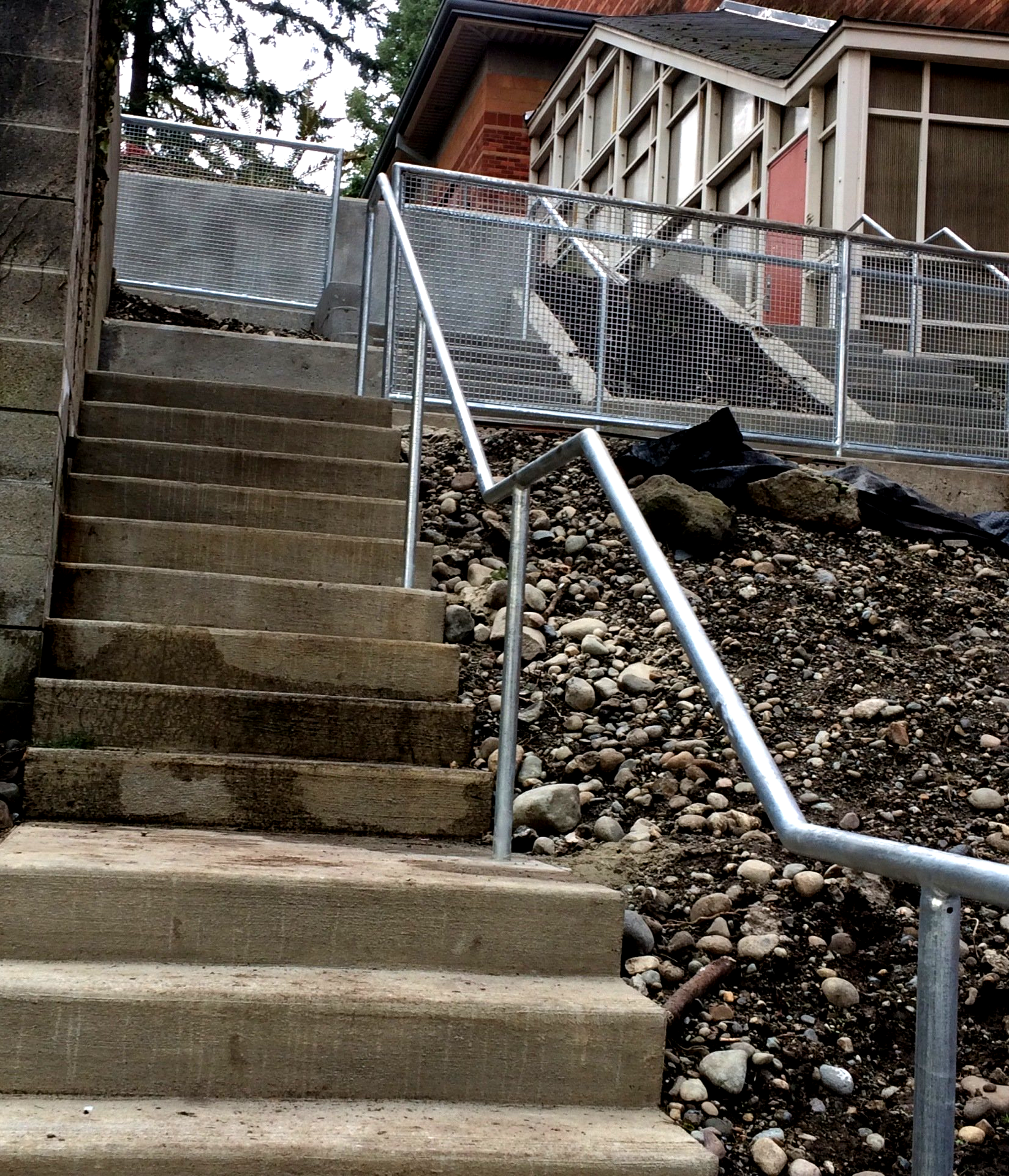 Steep outdoor concrete stairs with metal handrails beside a house and rocky hillside