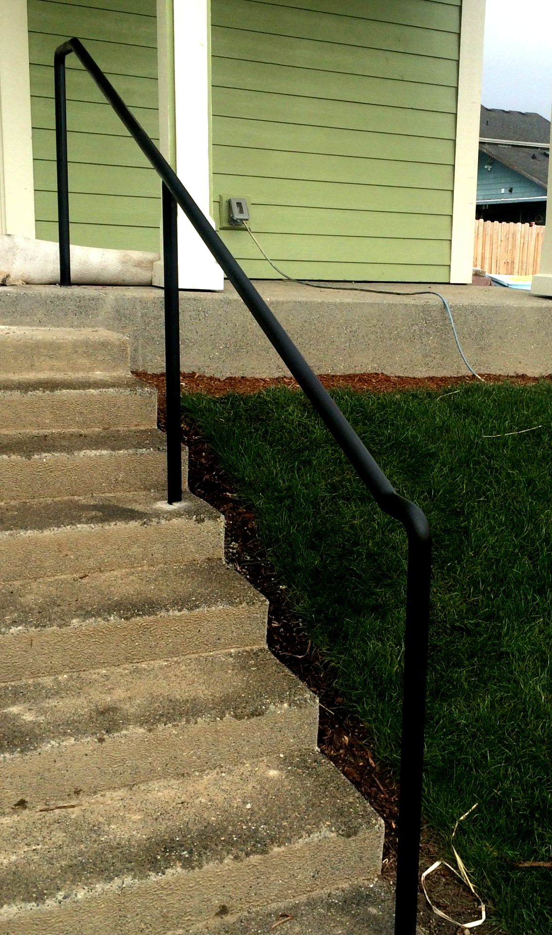 Concrete stairs with a black metal handrail beside a green house exterior