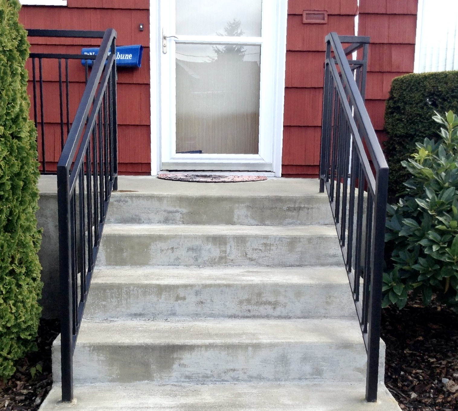 Concrete steps with black handrails leading to a white door on a red house.