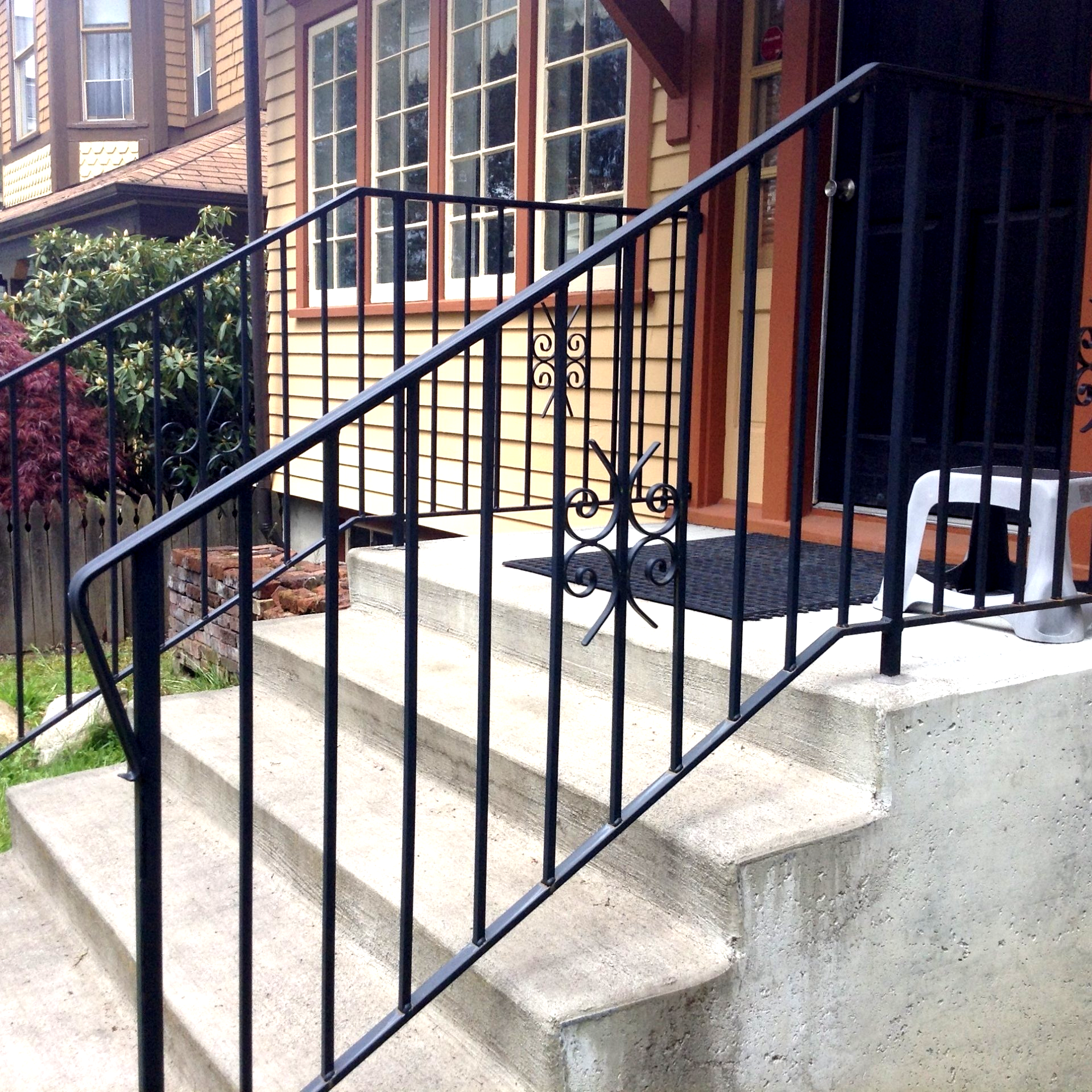 Black metal handrail beside concrete front steps leading to a brick house porch