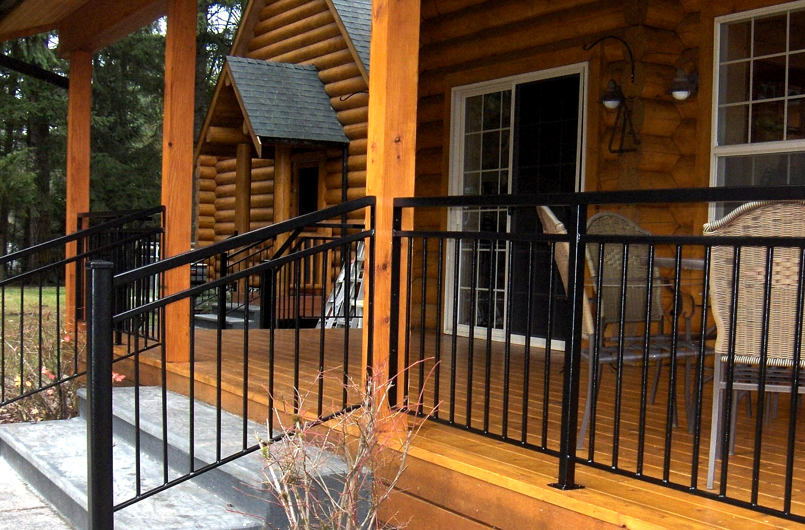 Black metal porch ramp and railing beside a log cabin with wooden siding and a sliding glass door