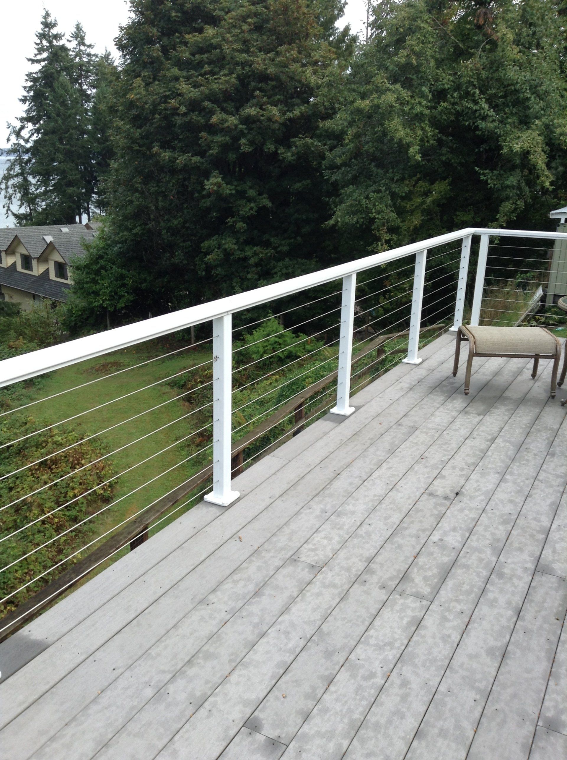 Wooden deck with white cable railing overlooking trees and a house