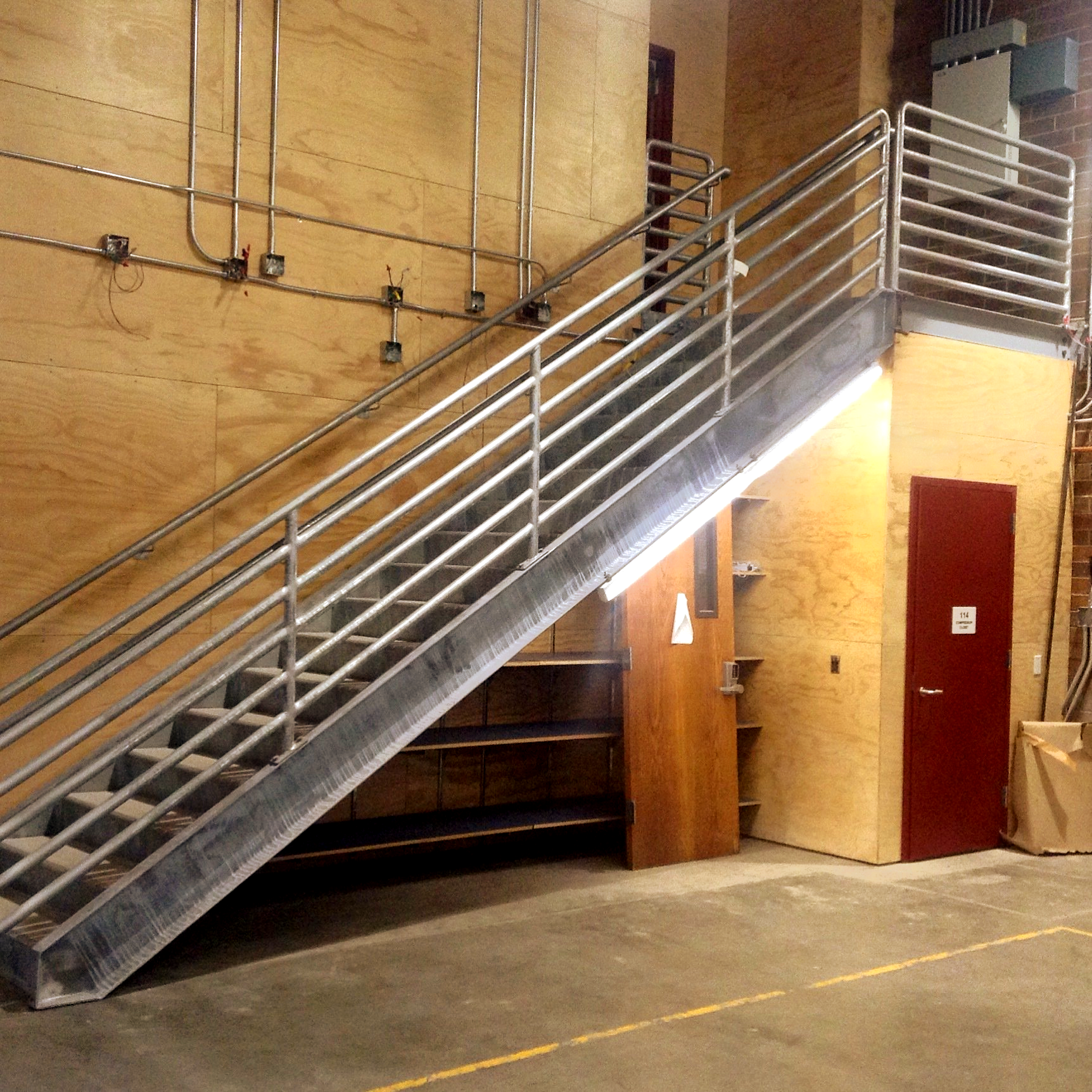 Metal staircase with silver railings in an industrial warehouse interior, beside a red door and tan wall.