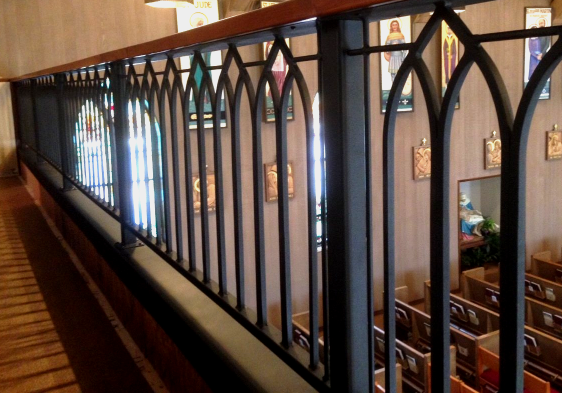 Church balcony railing with pointed arches overlooking pews below