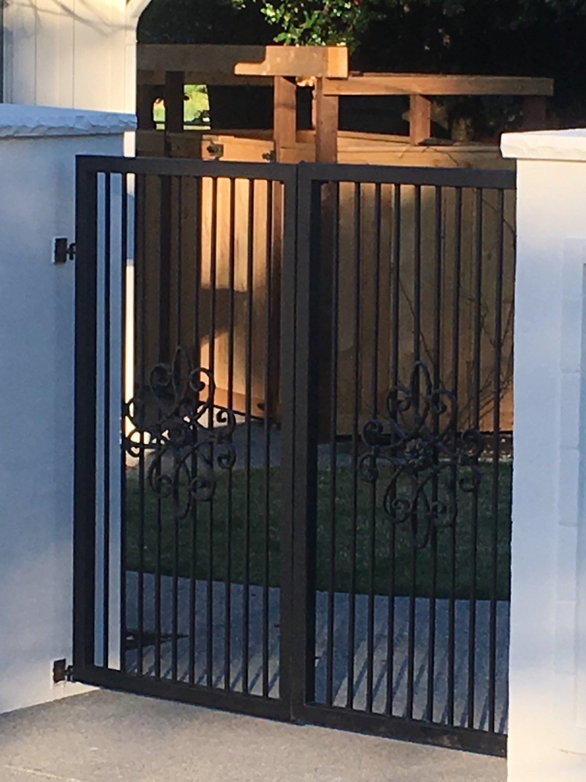 Black metal gate in front of a house with a wooden fence and small garden.