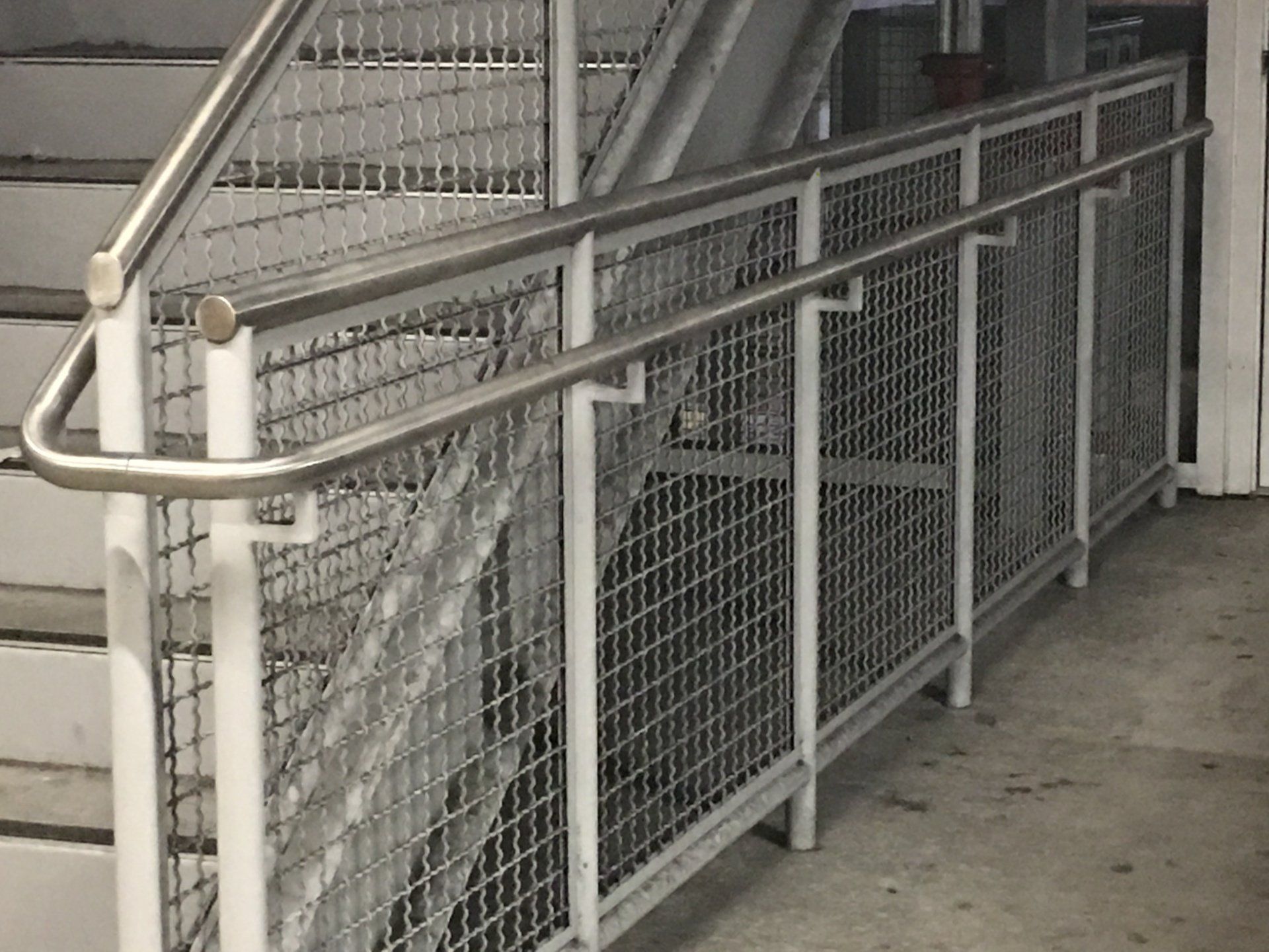 Metal ramp with railings and mesh panels beside stairs in an indoor building corridor