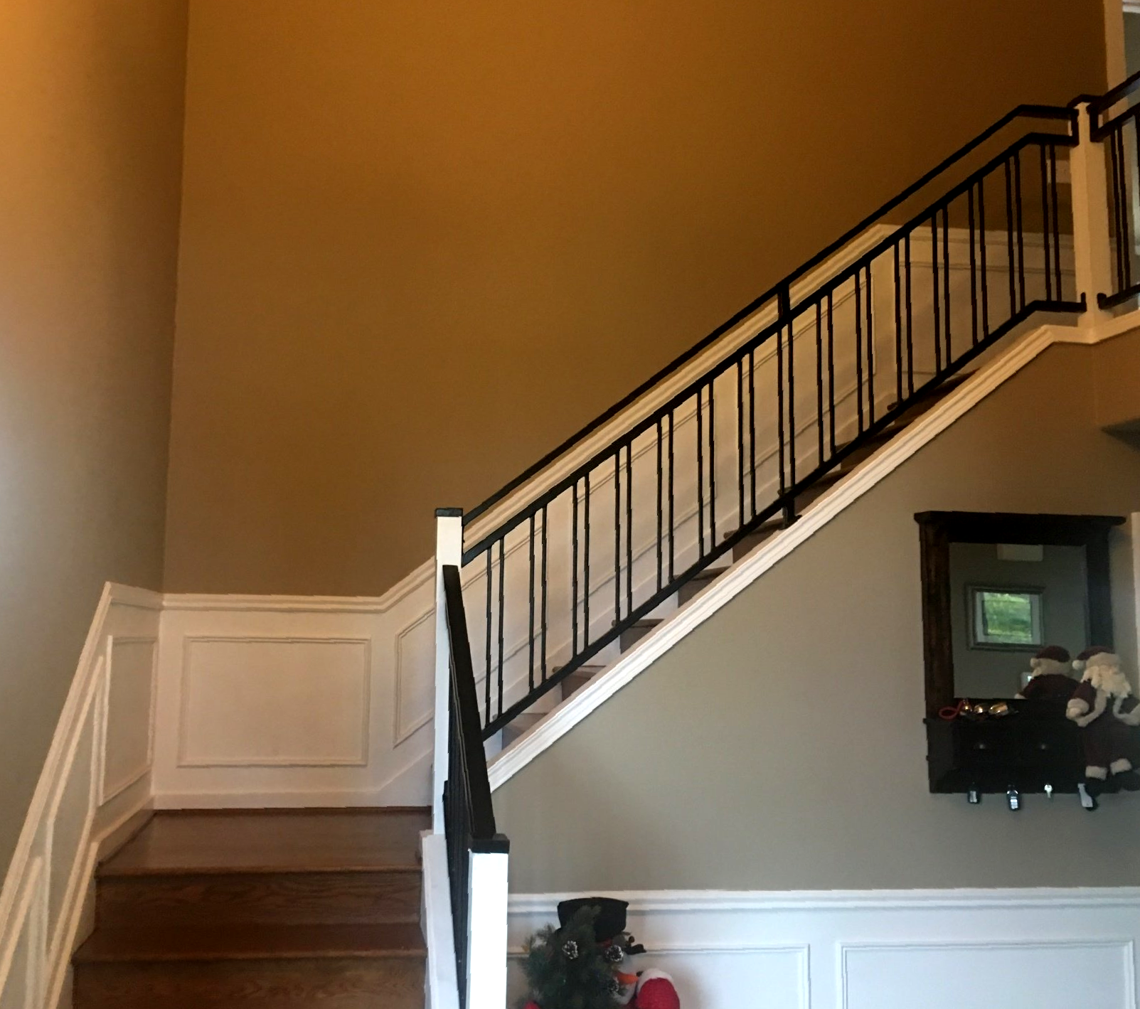 Interior staircase with dark railing, white wainscoting, and a wall mirror in a tan hallway.