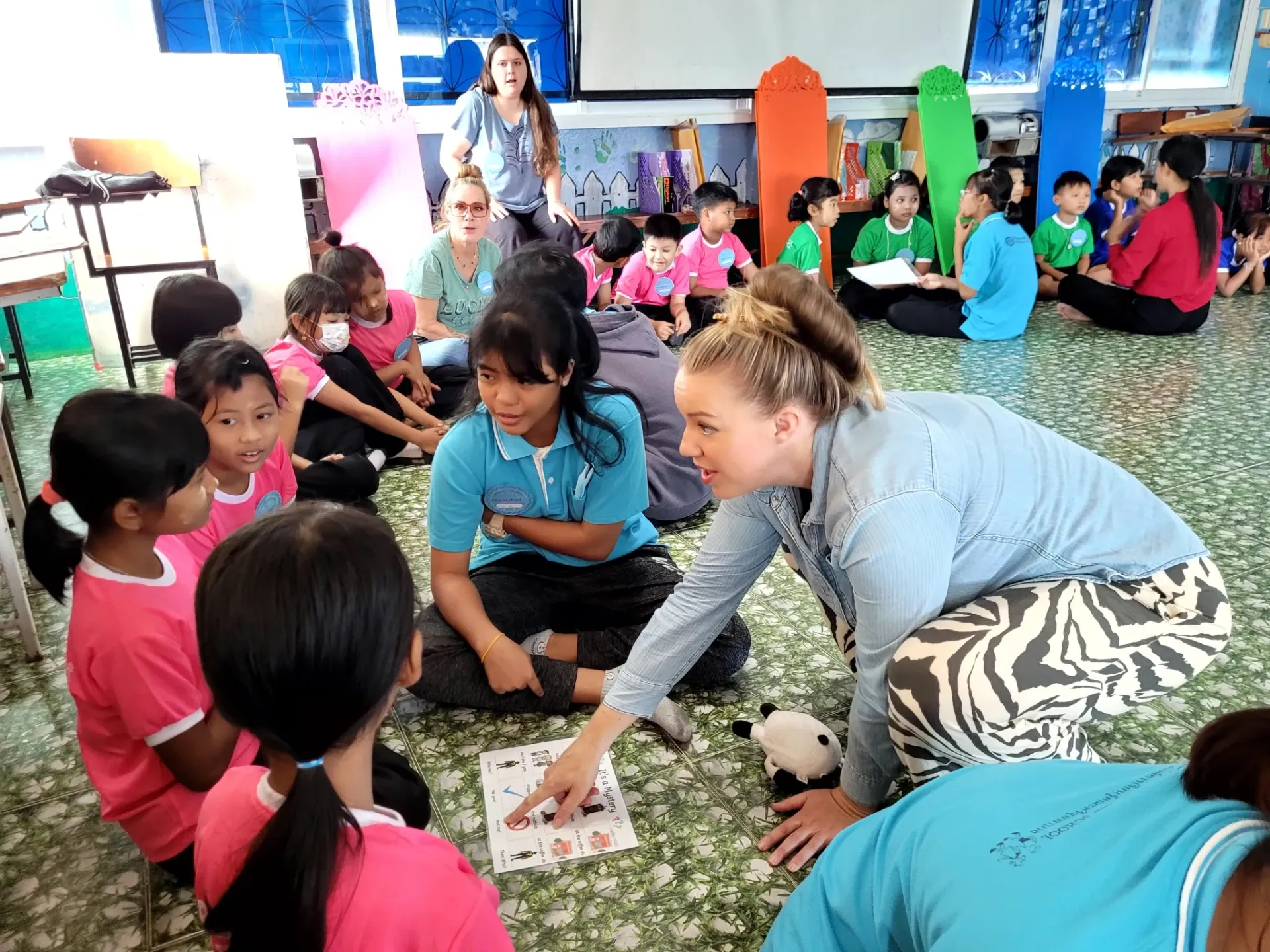 A group of children are sitting on the floor with a woman pointing at something