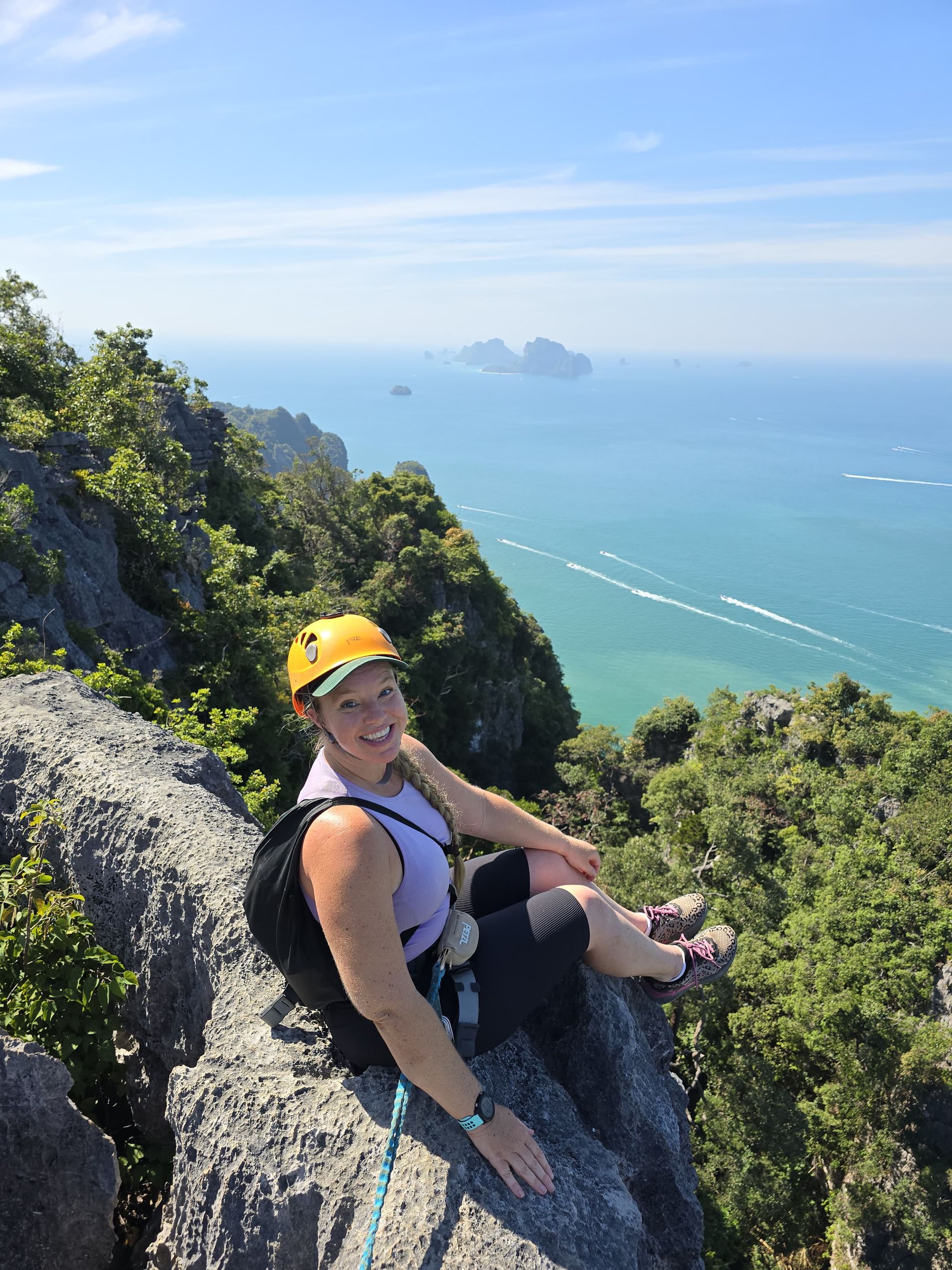 A woman is sitting on the edge of a cliff overlooking the ocean