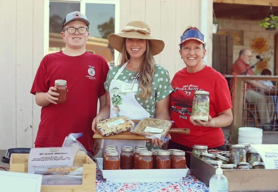 A group of people are standing around a table holding jars of food.