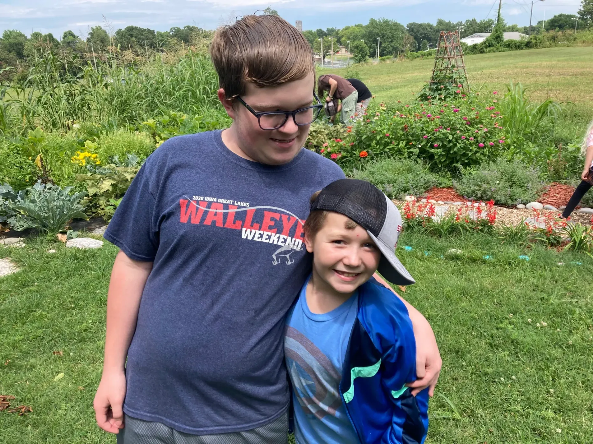 Two young boys are posing for a picture in a garden with one wearing a walleye shirt