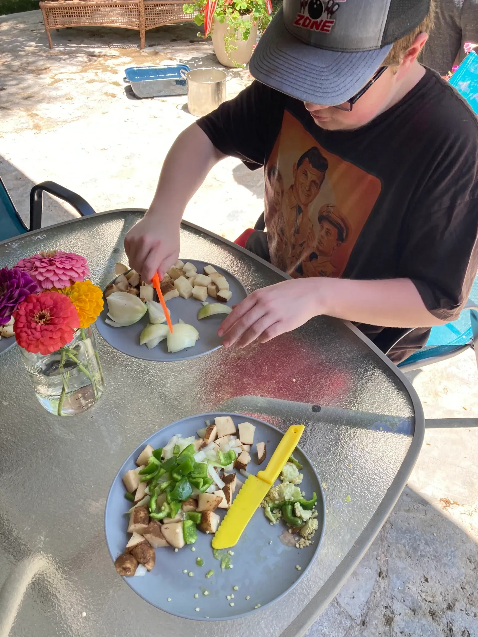 A boy wearing a hat is cutting vegetables on a table