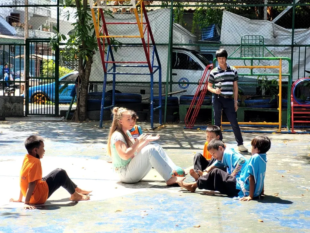 A woman sits on the floor with a group of children