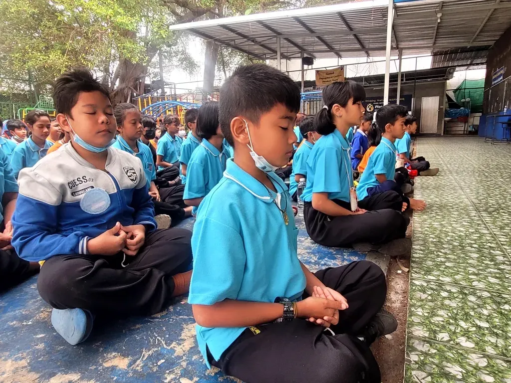 A group of children are sitting on the ground with their eyes closed.