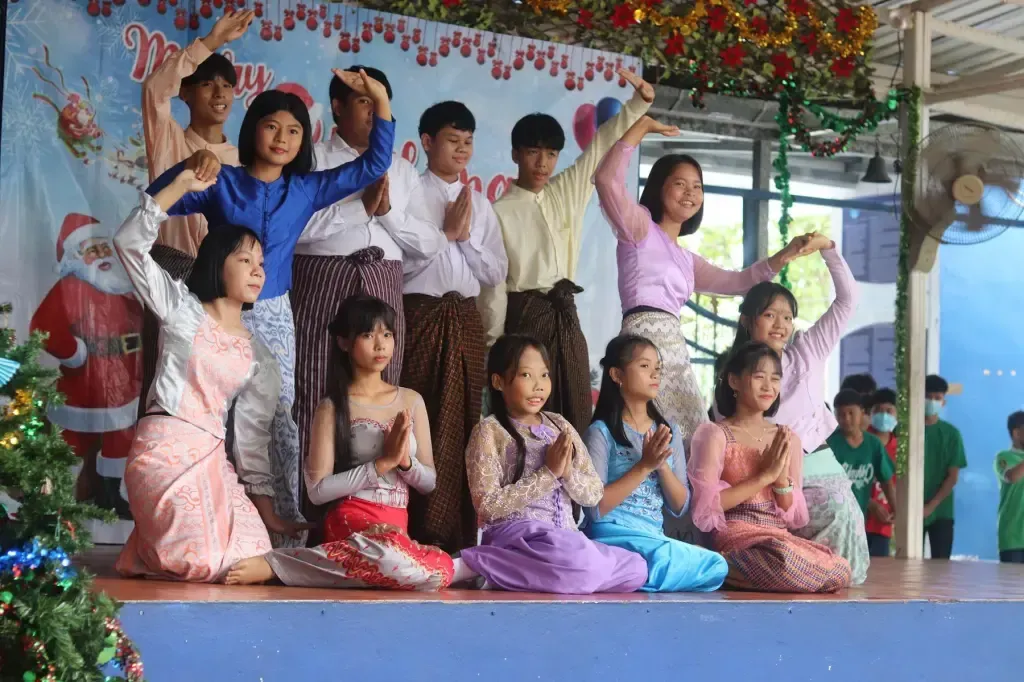 A group of children are dancing on a stage in front of a christmas tree.