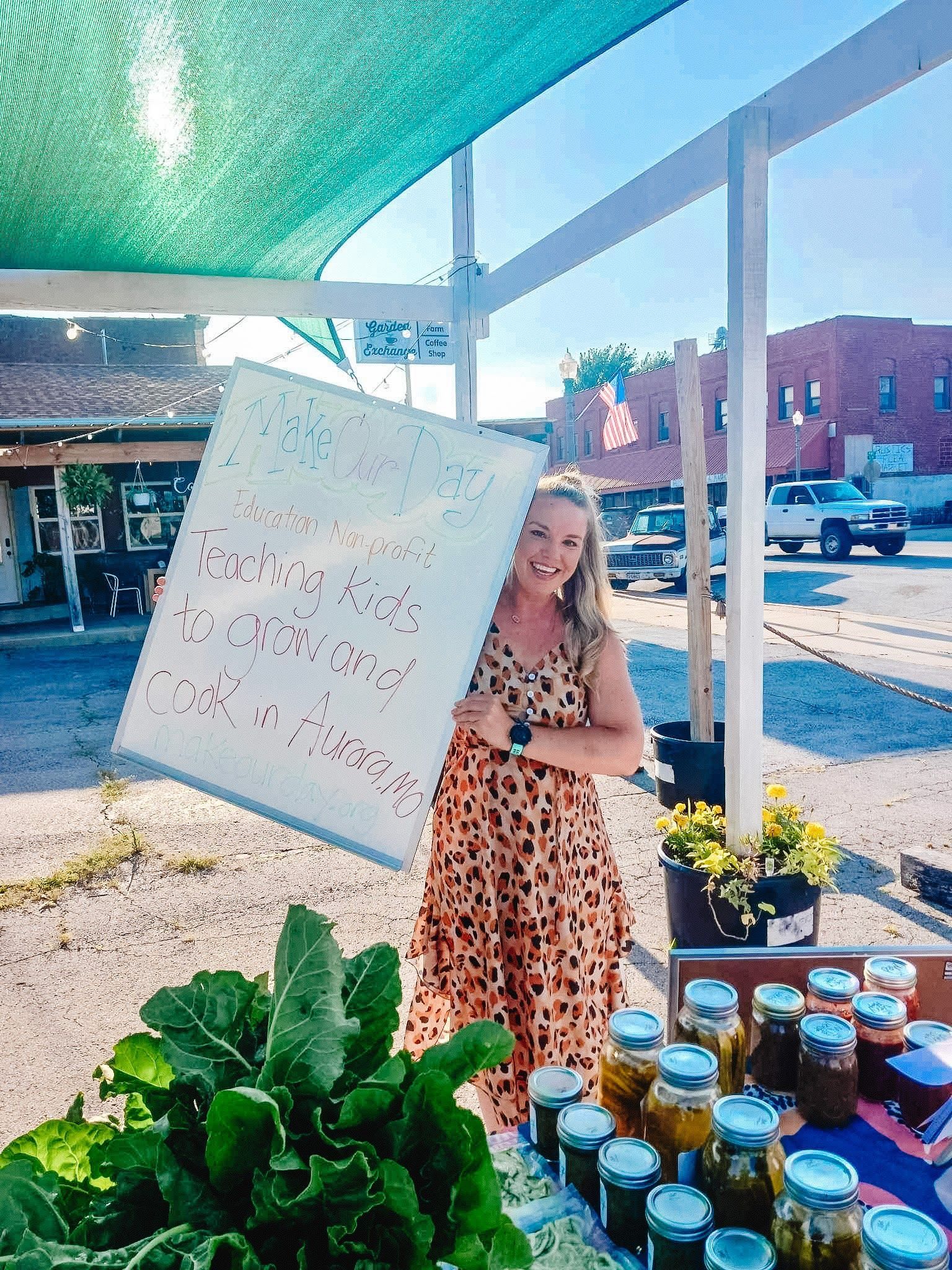 A woman is standing in front of a table with jars of pickles.